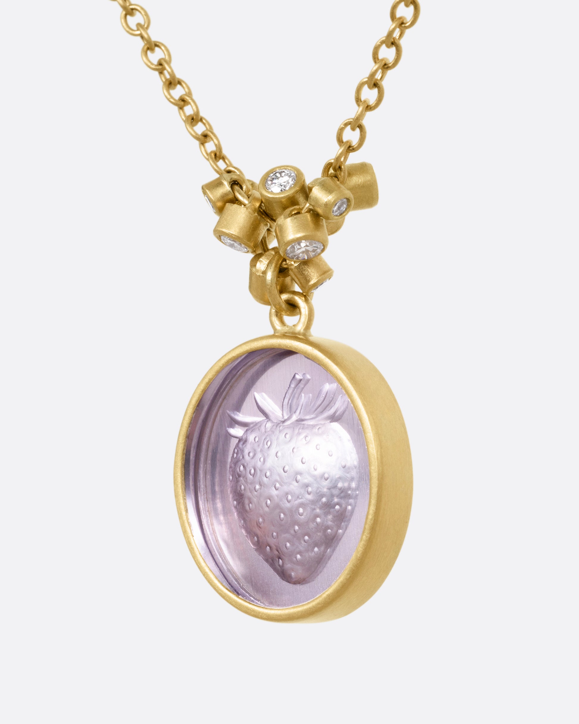 A yellow gold pendant necklace with a amethyst with a hand carved strawberry and a cluster of diamond charms, shown from the side.