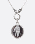 A silver pendant necklace with a hand carved hamsa in a bezel set quartz, hanging from a dual headed, diamond eyed snake. Shown from the front.