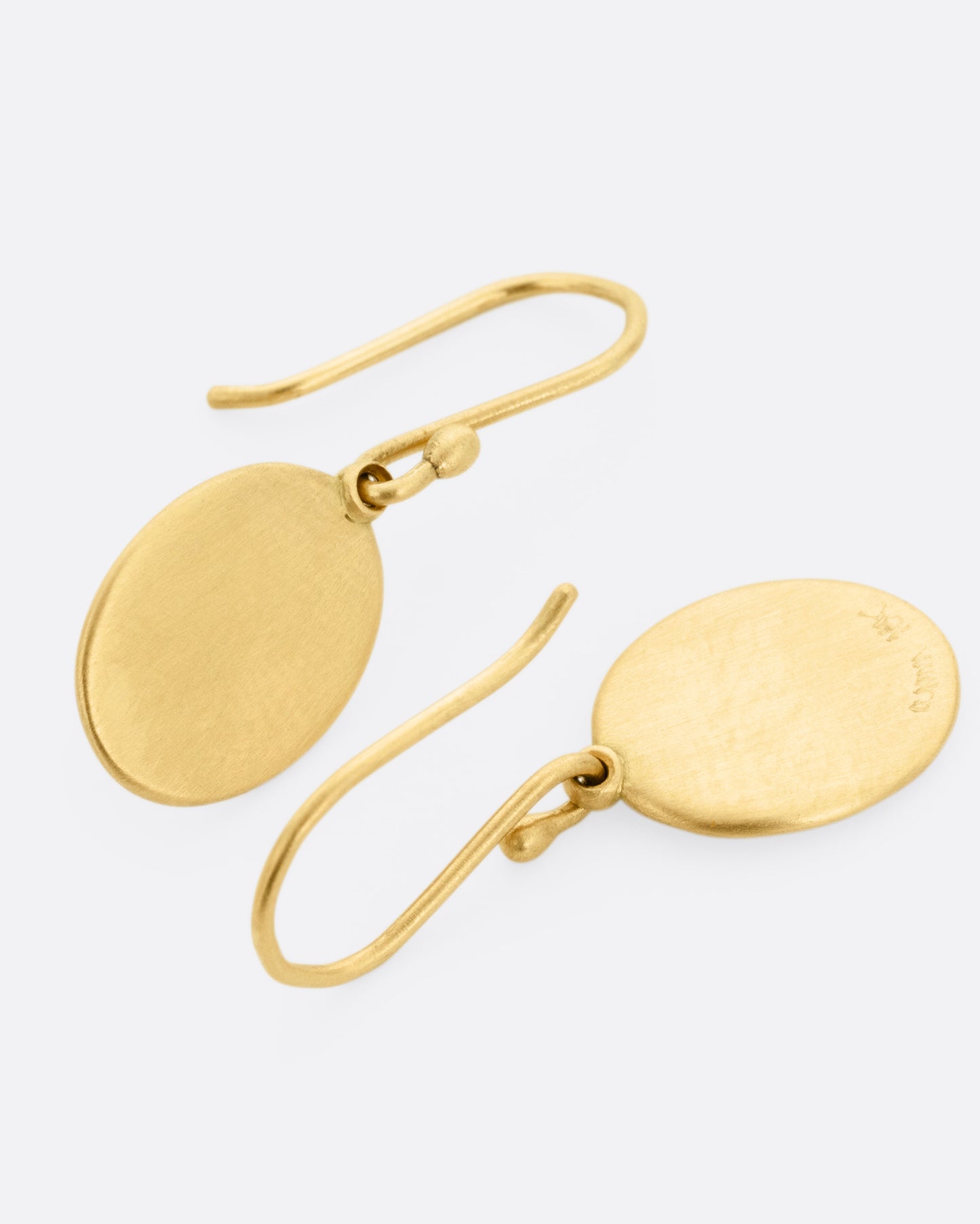 A pair of yellow gold hook earrings with oval dangles, shown lying flat.