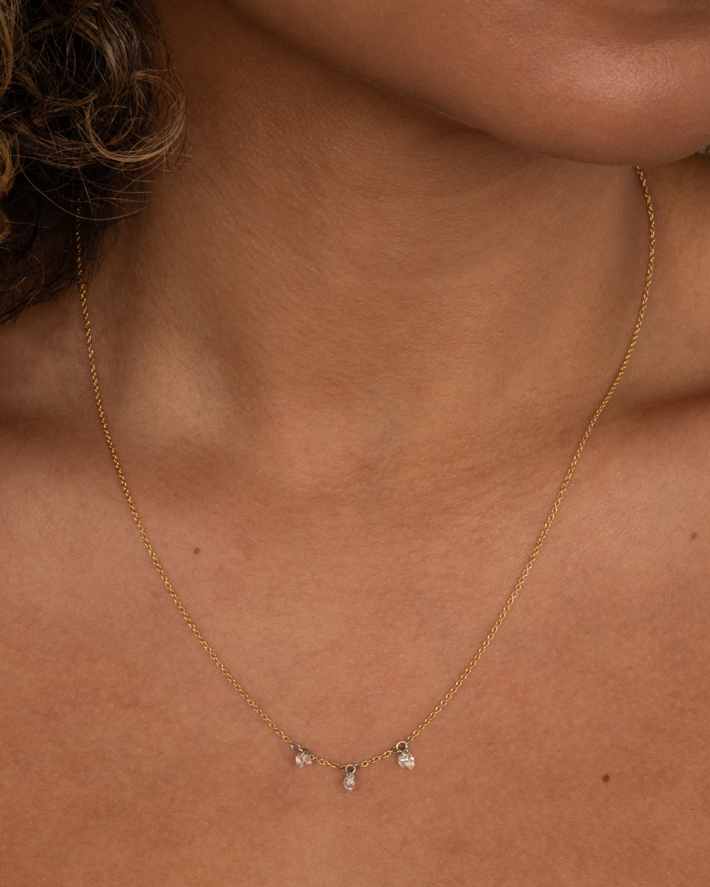 A yellow gold cable chain necklace with three stations of two marquise diamonds. View worn around the neck.