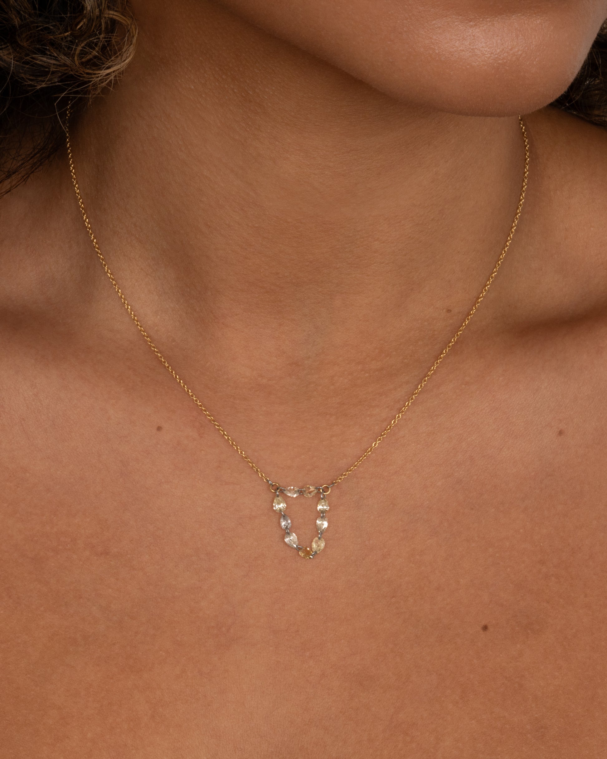 A close up of a yellow gold cable chain necklace with a loop of nine rose cut diamonds at the center. Shown worn.