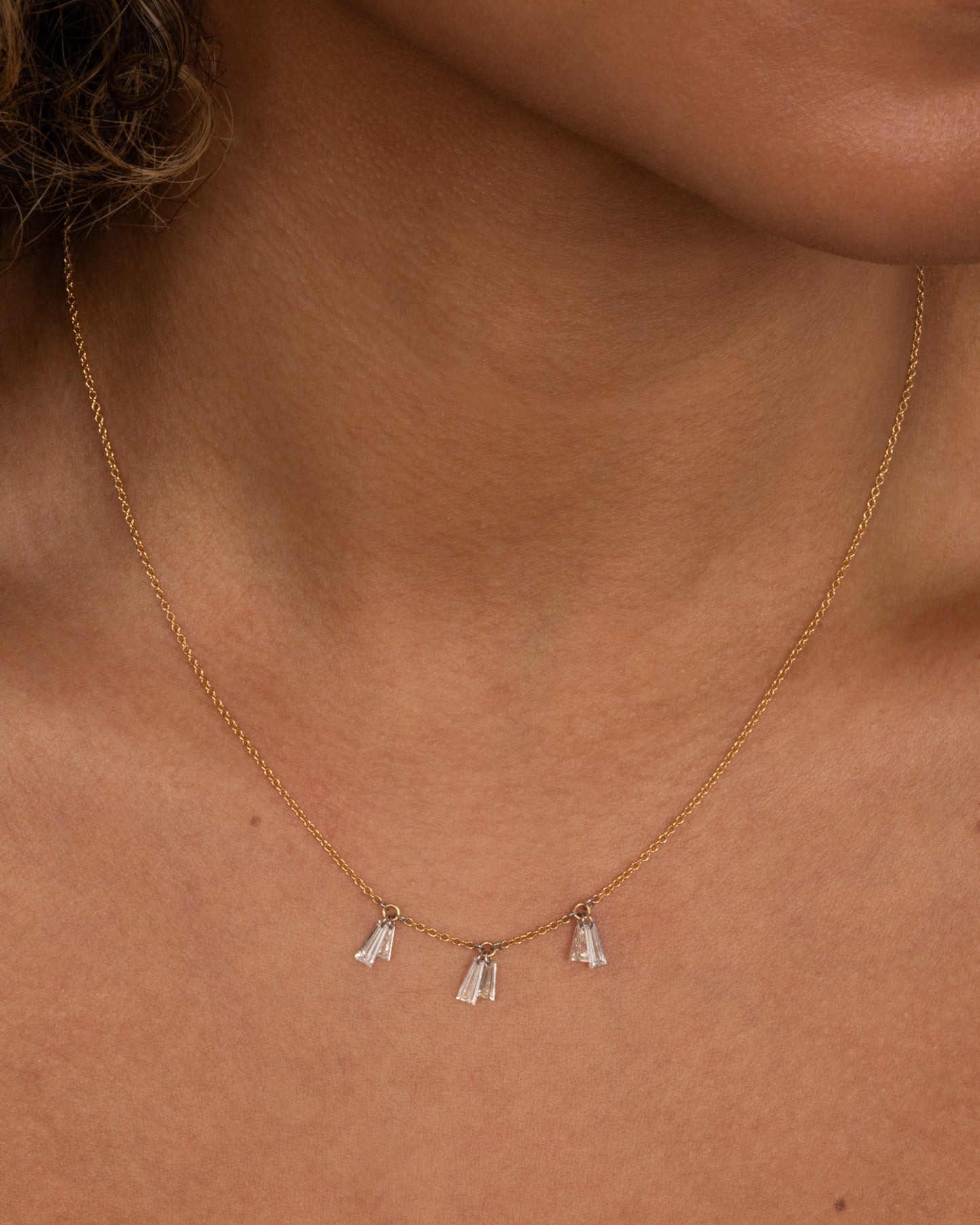 A yellow gold cable chain necklace with six baguettes hanging on platinum jump rings. View from the front.