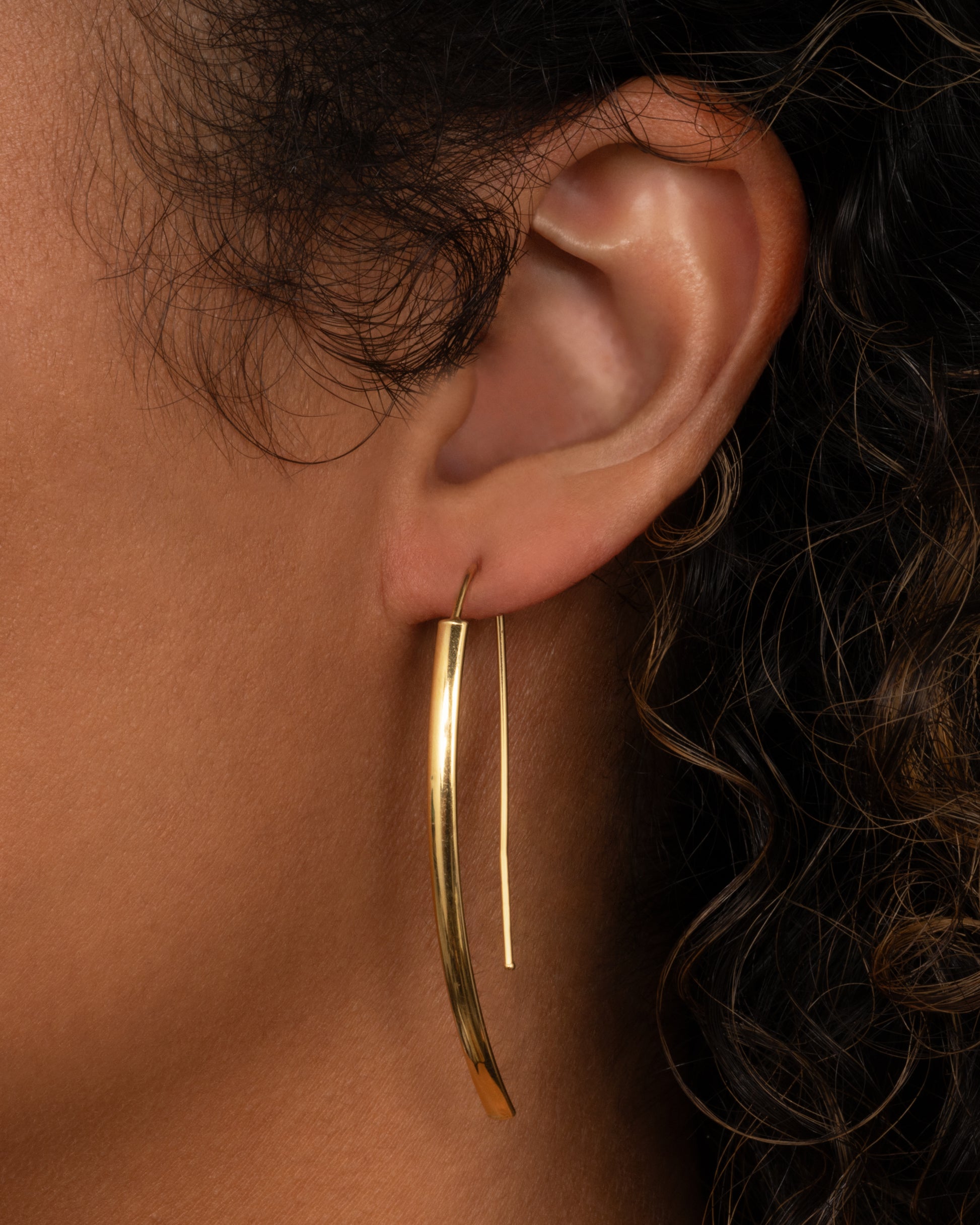 A yellow gold threader half hoop earring shown on a person.