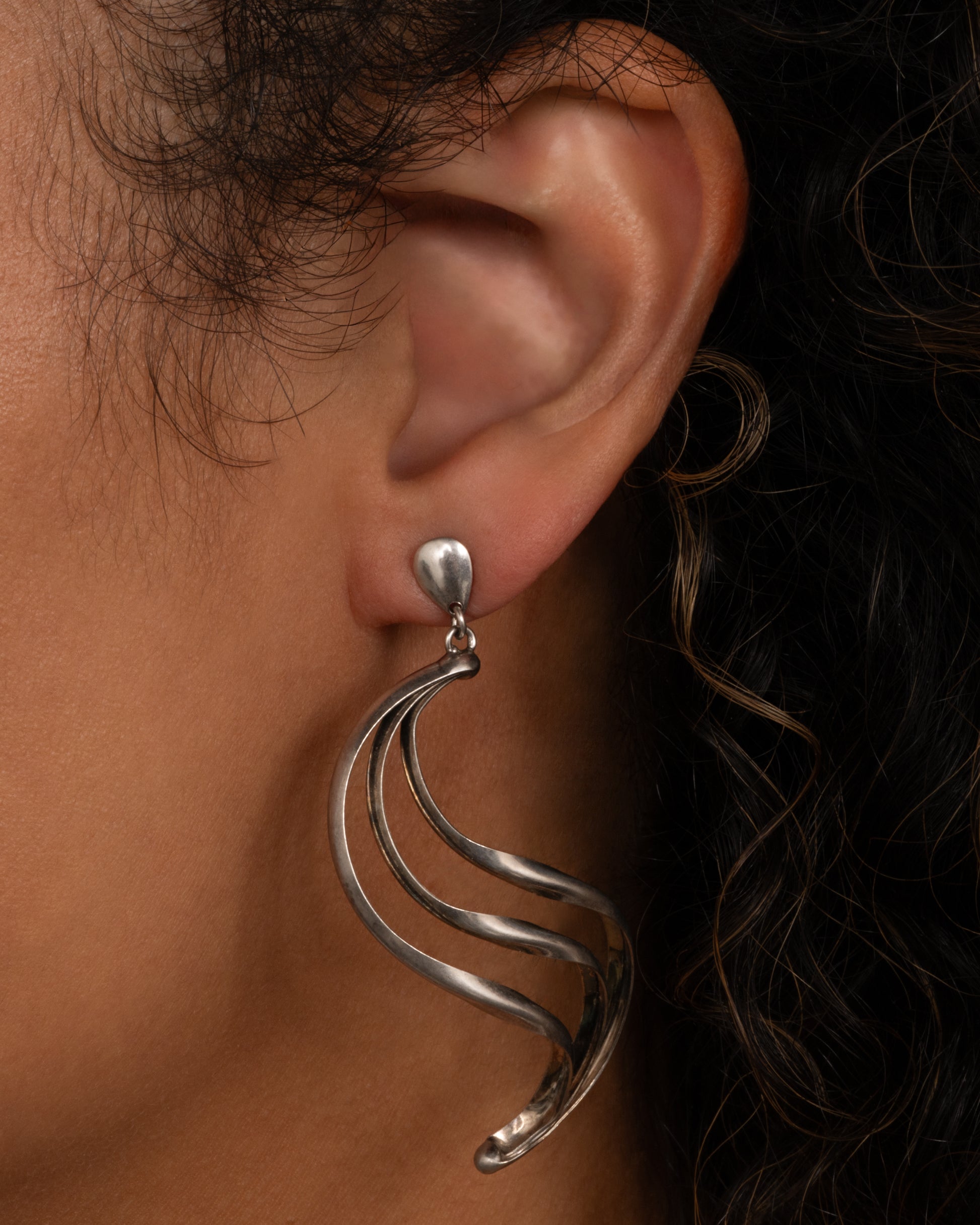 Silver dangle earrings with stud tops and three layers of silver ribbons in an S shape. Shown worn.