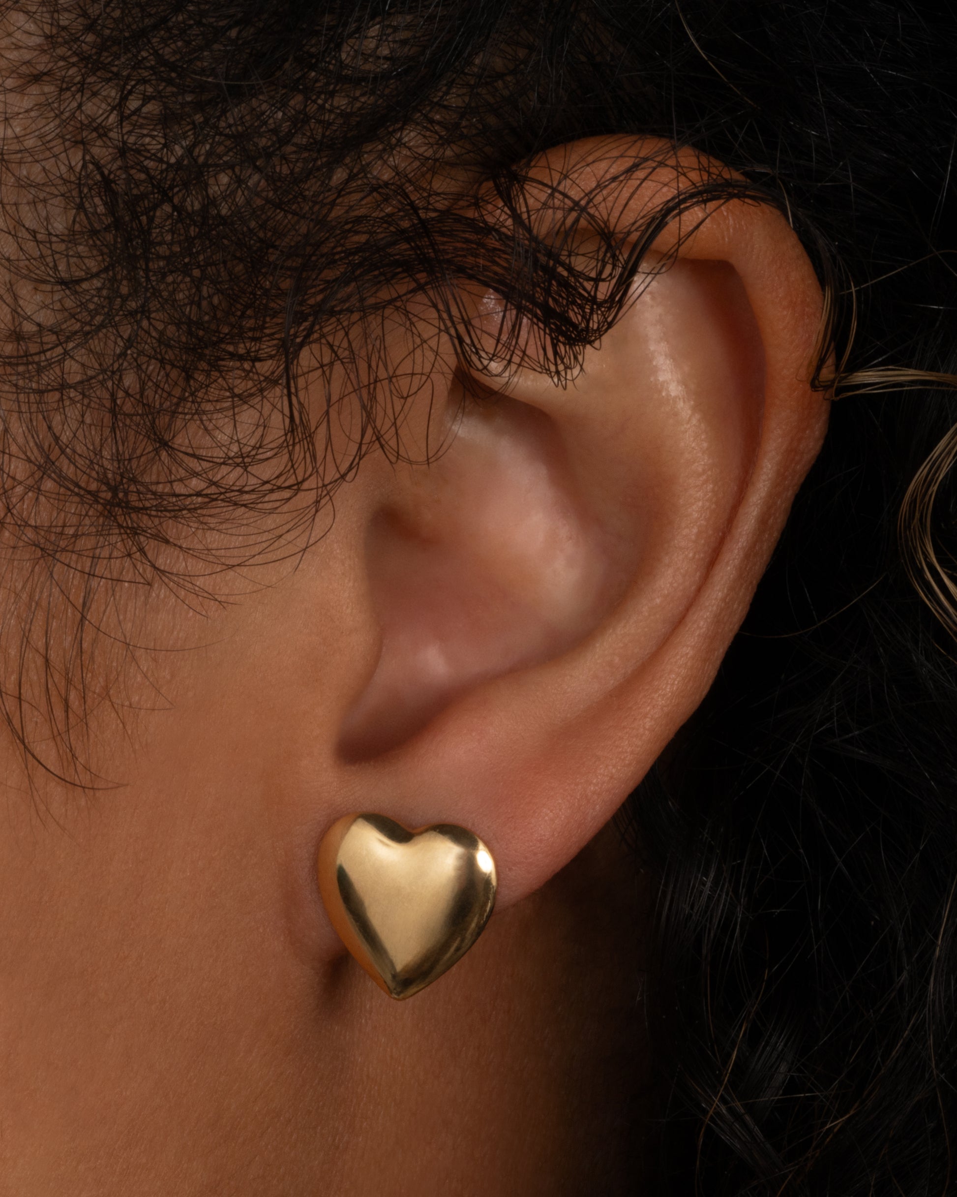 A yellow gold heart-shaped stud earring, shown from the front on a person.