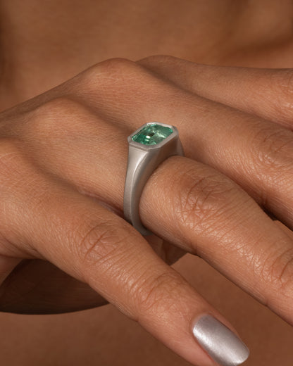 A platinum signet ring with an emerald, shown on a hand.