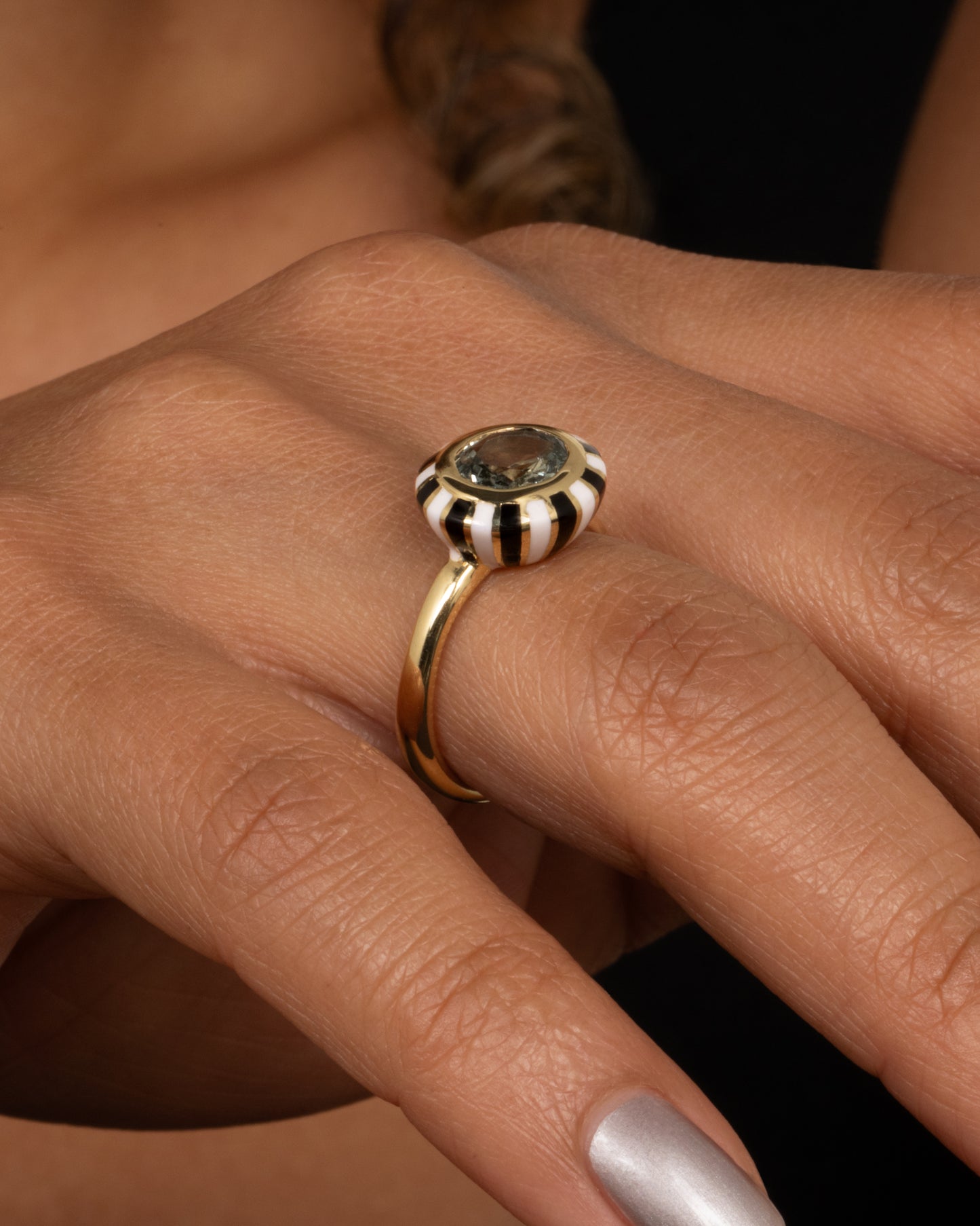 A yellow gold ring with an enamel checkerboard pattern around a green sapphire, shown on a hand.