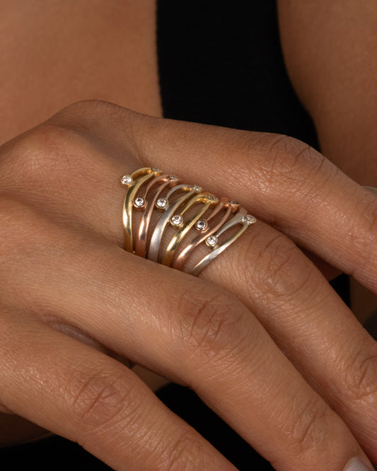 Round bezel set diamonds freckle the face of this A yellow, rose, and white gold layered ring with open cutouts, a tapered back, and round bezel set diamonds scattered throughout the front. Shown worn