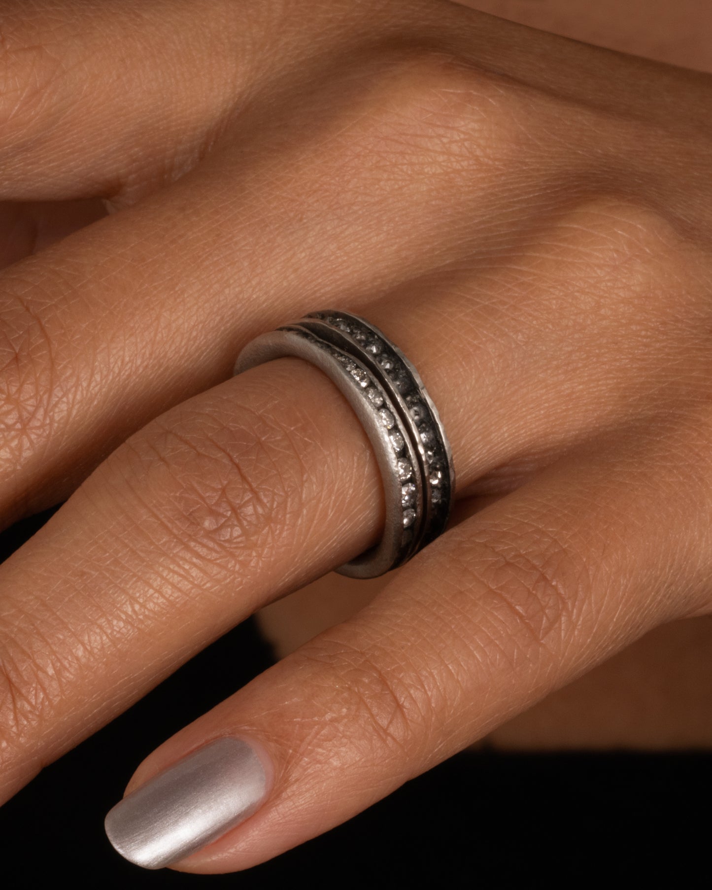 A nonuniform platinum ring with a darkened channel filled with diamonds. Shown worn.
