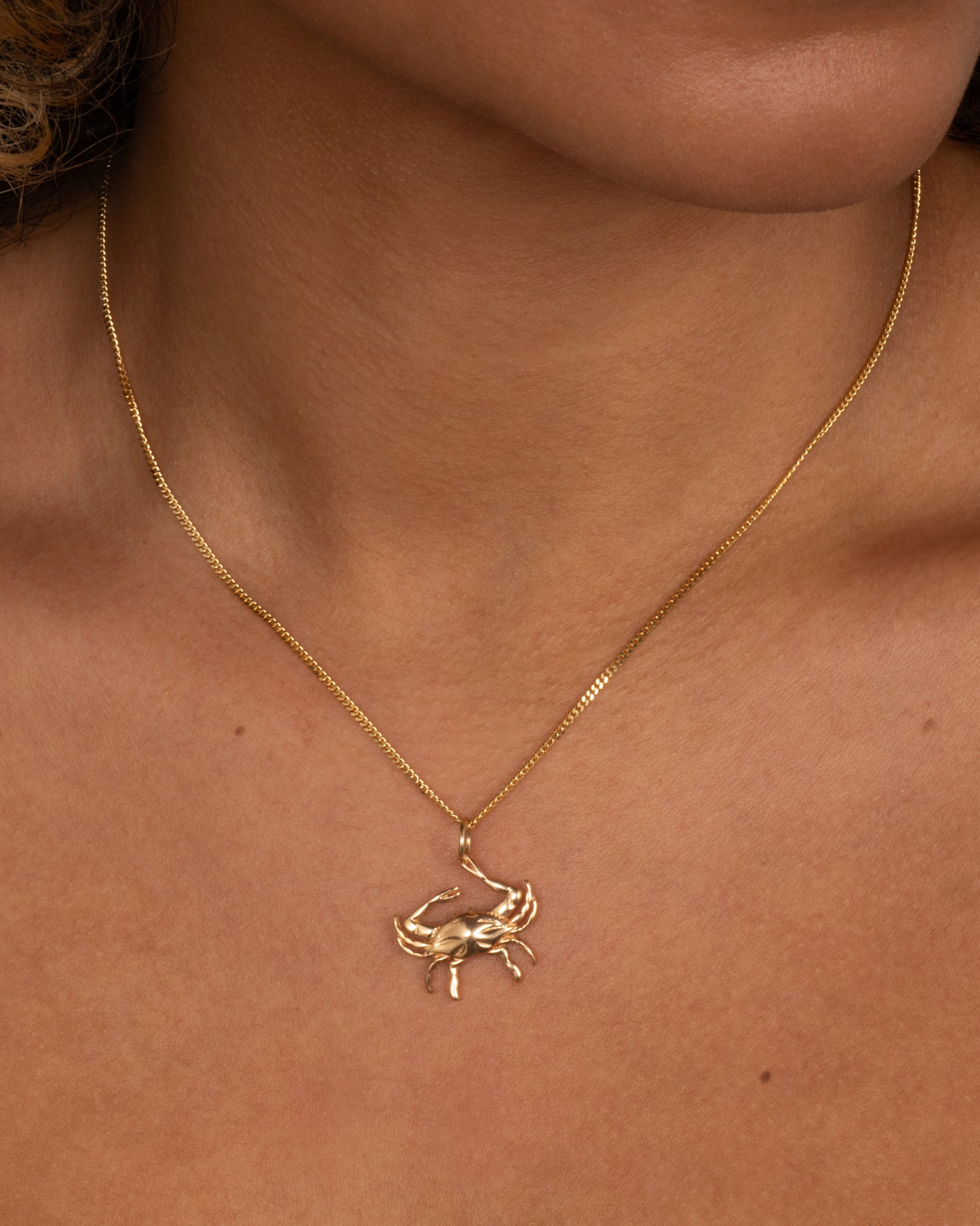 A yellow gold crab pendant grasping onto a jump ring with one claw. Shown worn.