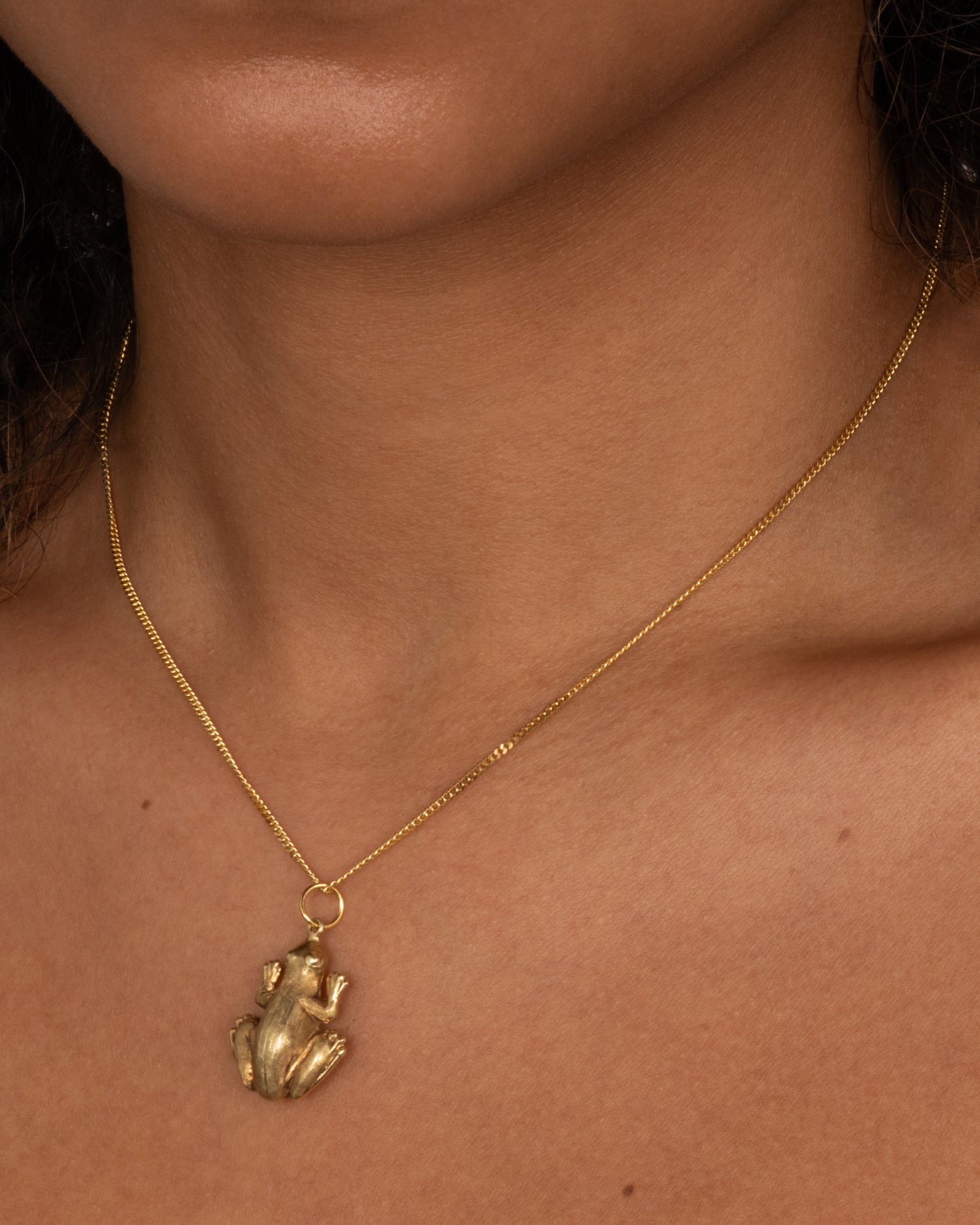 A yellow gold frog pendant shown worn.