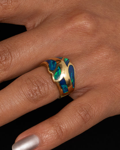 A yellow gold ring with an abstract inlay of opal. Shown on a hand.