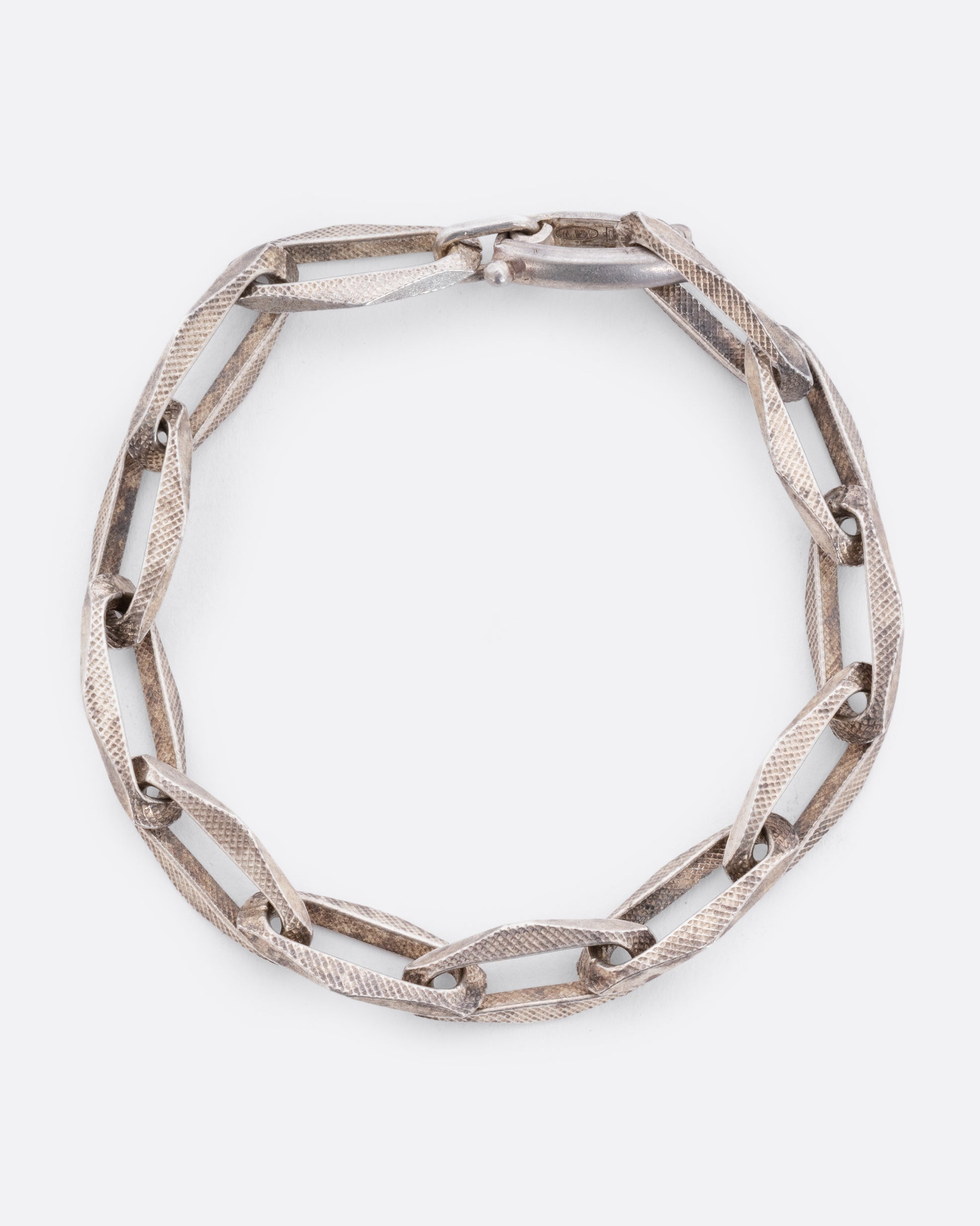 A sterling silver bracelet with textured geometric oval links. View closed, from above.