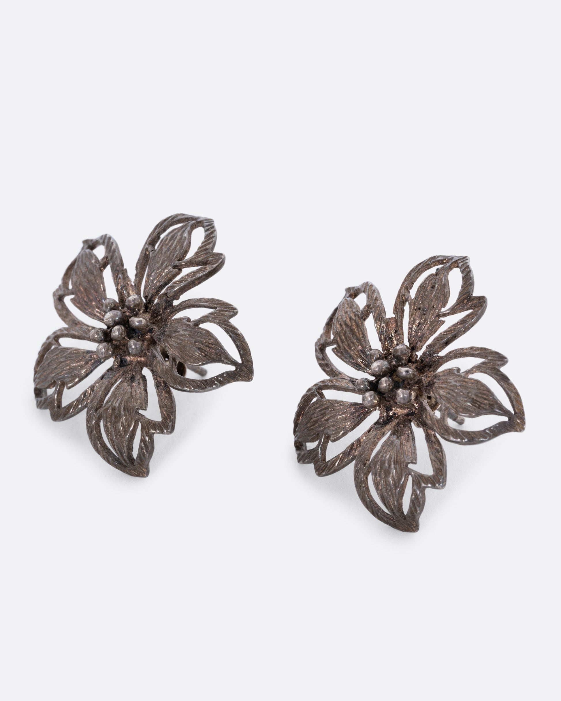 A pair of oxidized sterling openwork flower stud earrings. View from the side.