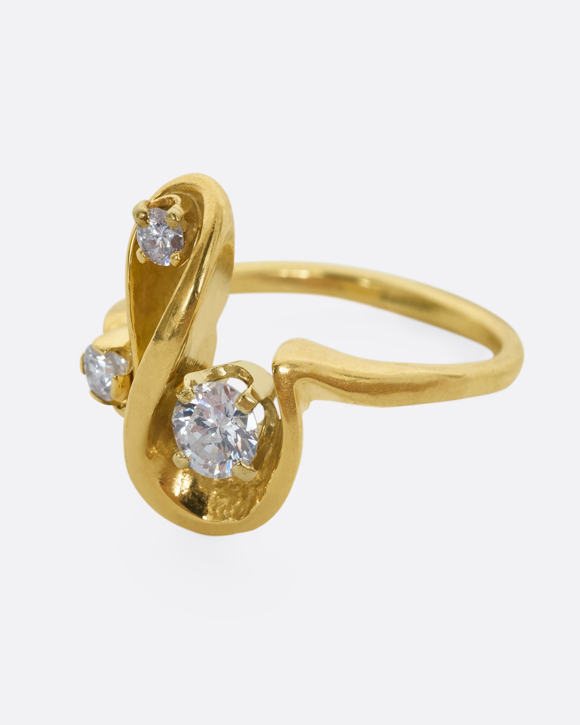 A yellow gold abstract swirl ring with three diamonds. View from the side.