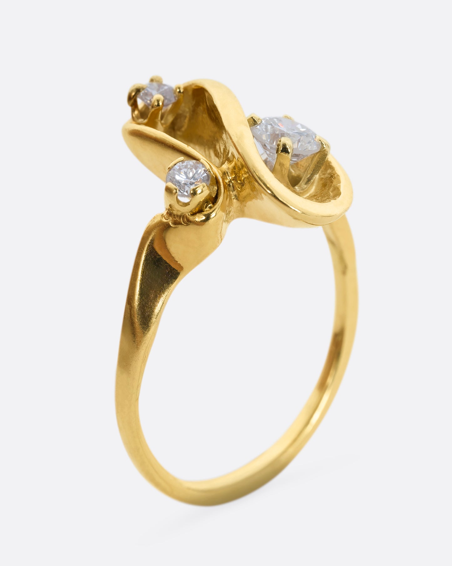 A yellow gold abstract swirl ring with three diamonds. View from the side, standing.