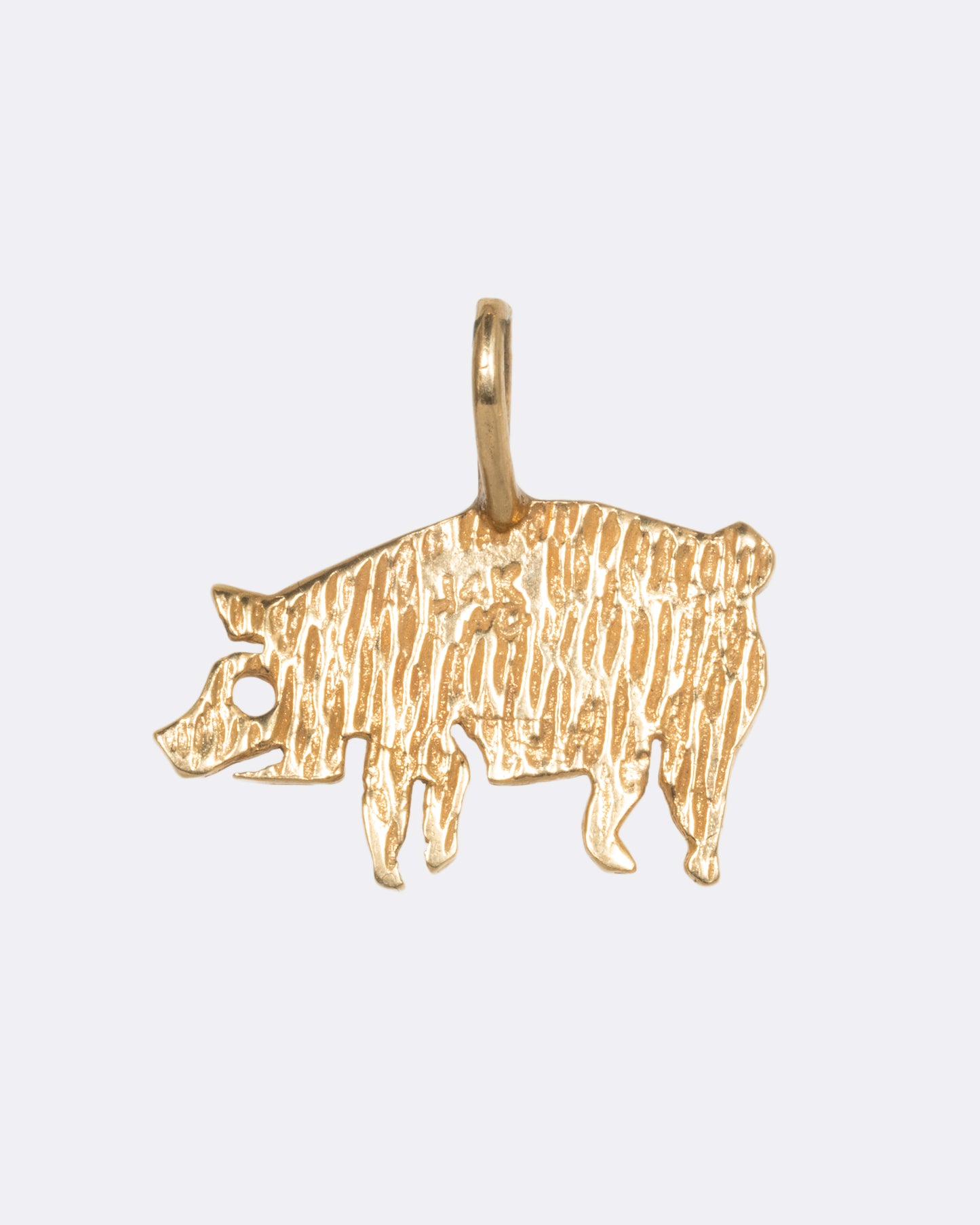 A yellow gold etched pig charm. View from the back.