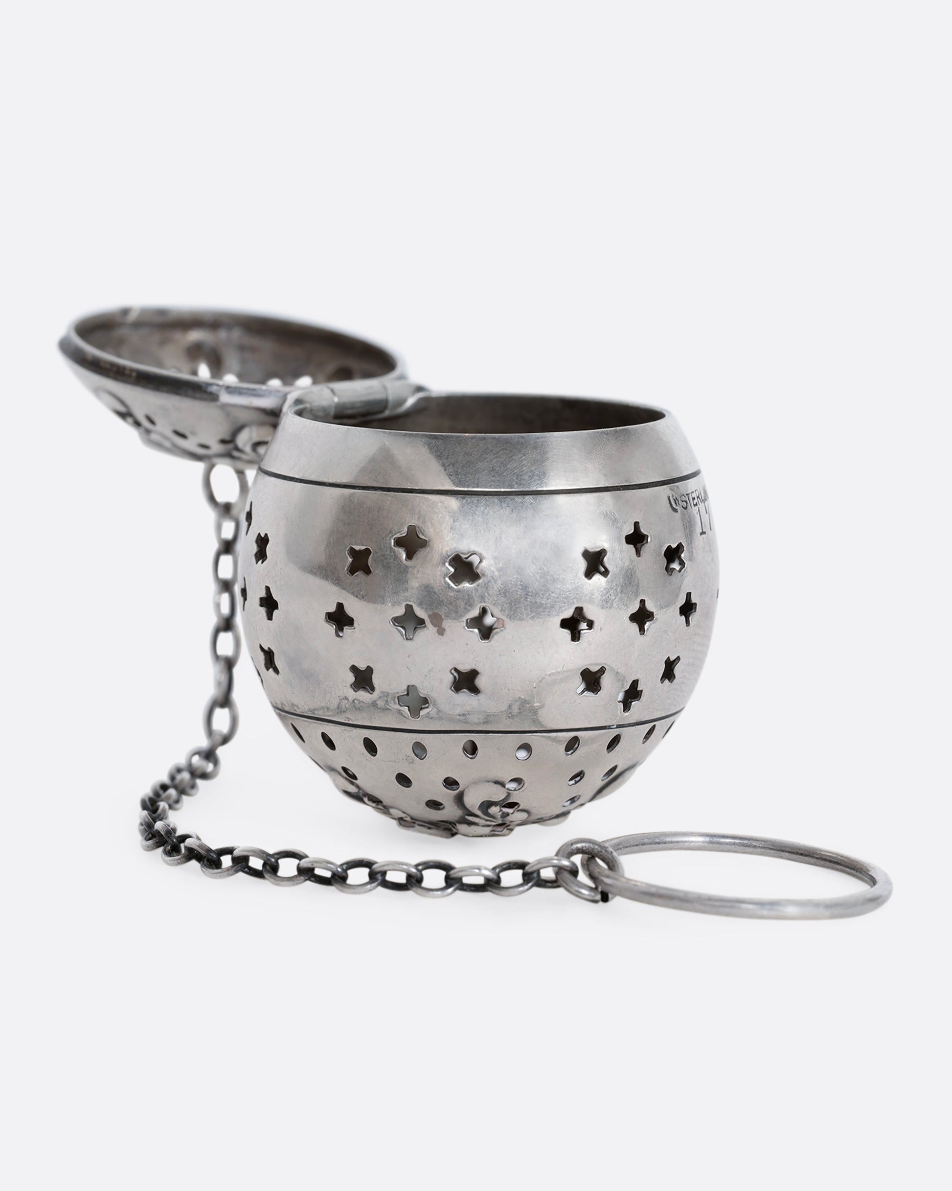 A sterling silver spherical tea infuser with botanical detail on lid. Shown open from the side.