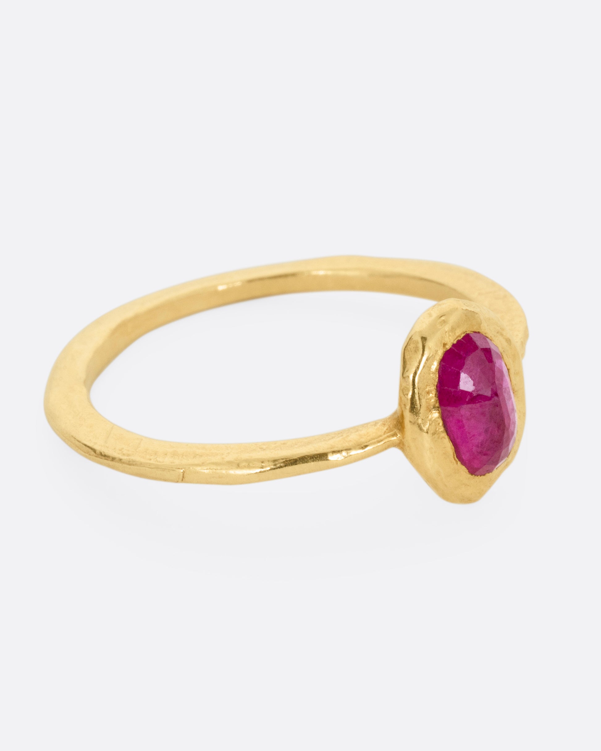 A yellow gold ring with a bezel set ruby, shown from the side.