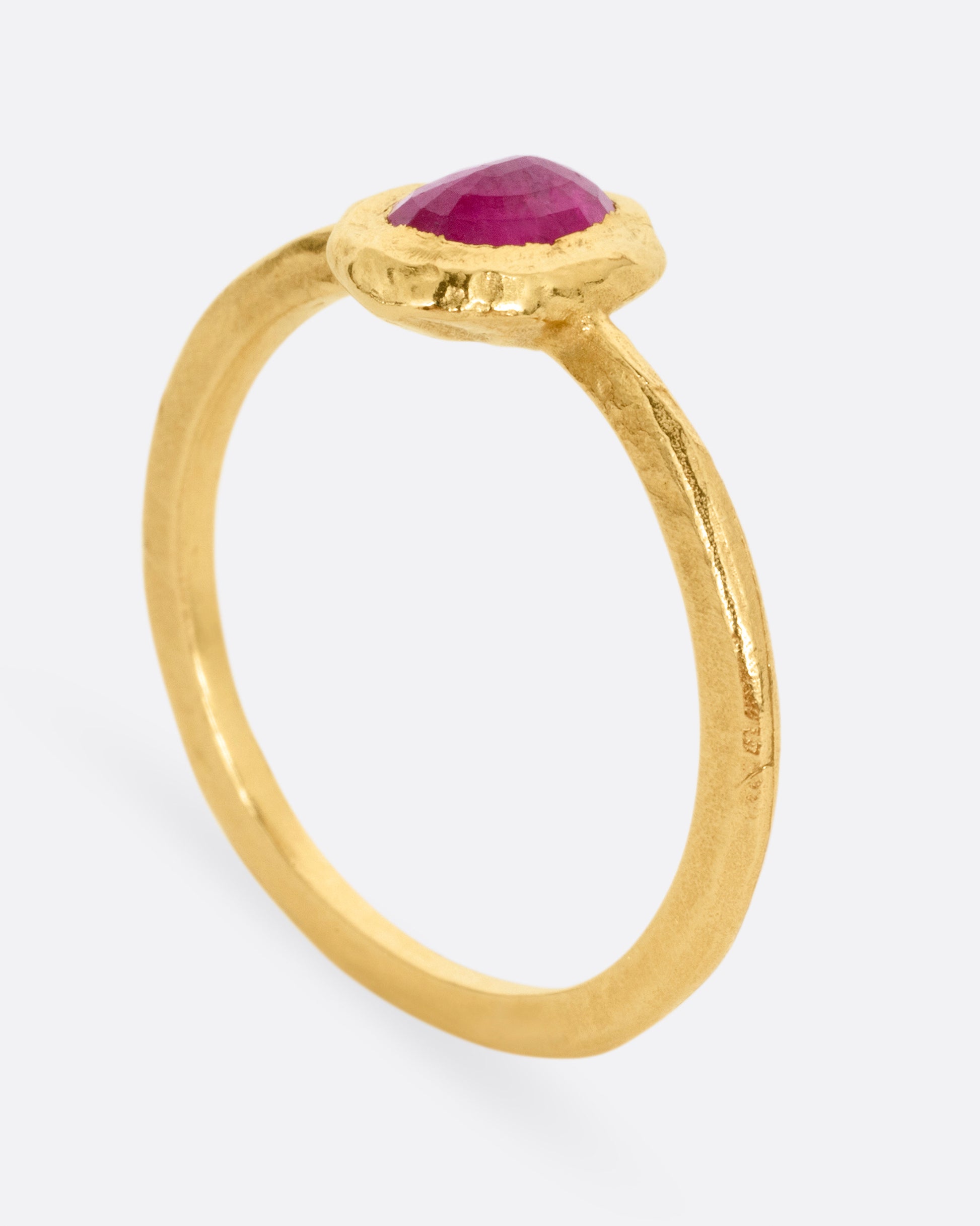 A yellow gold ring with a bezel set ruby, shown standing up from the side.