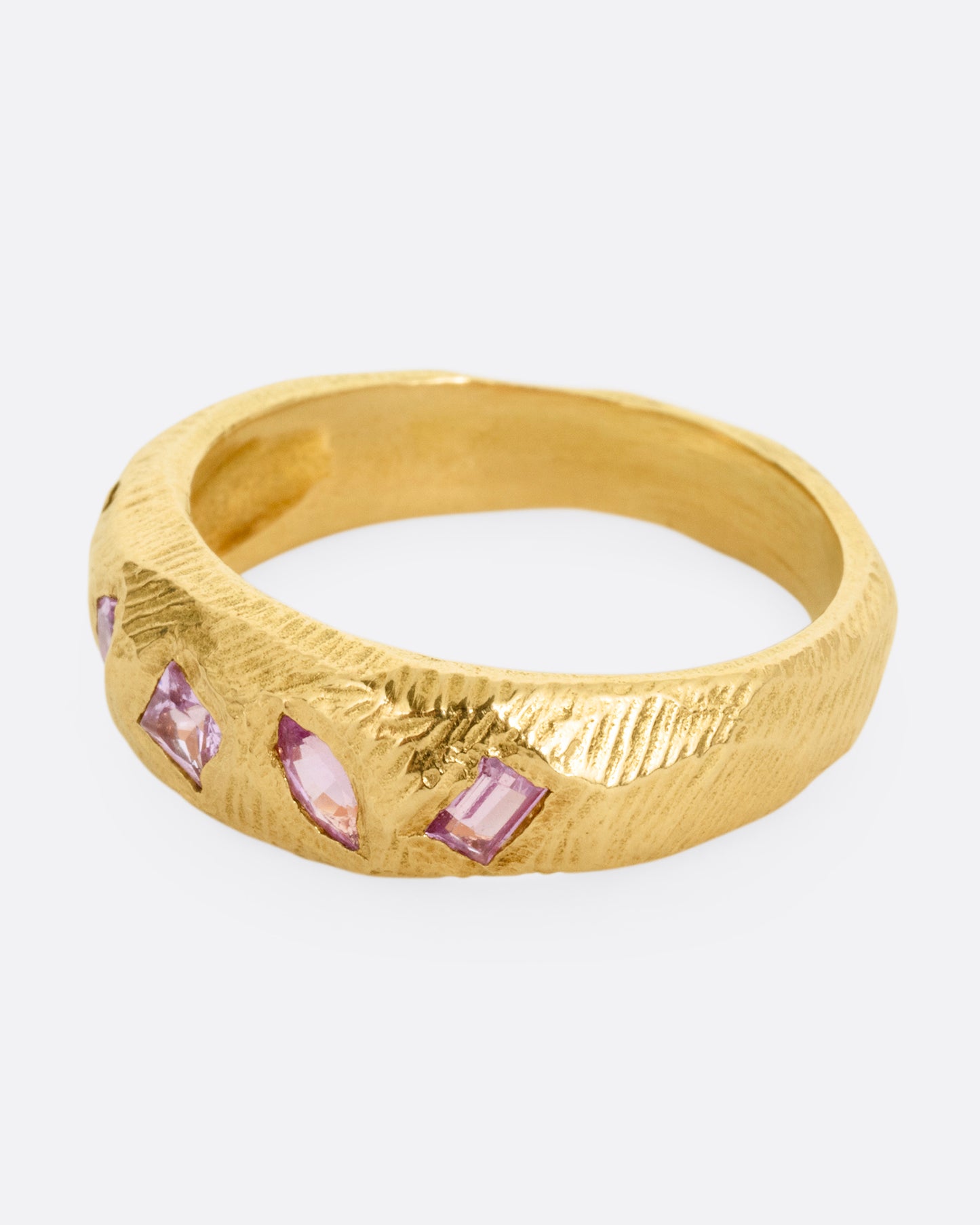 A yellow gold band with five pink sapphires, shown from the side.