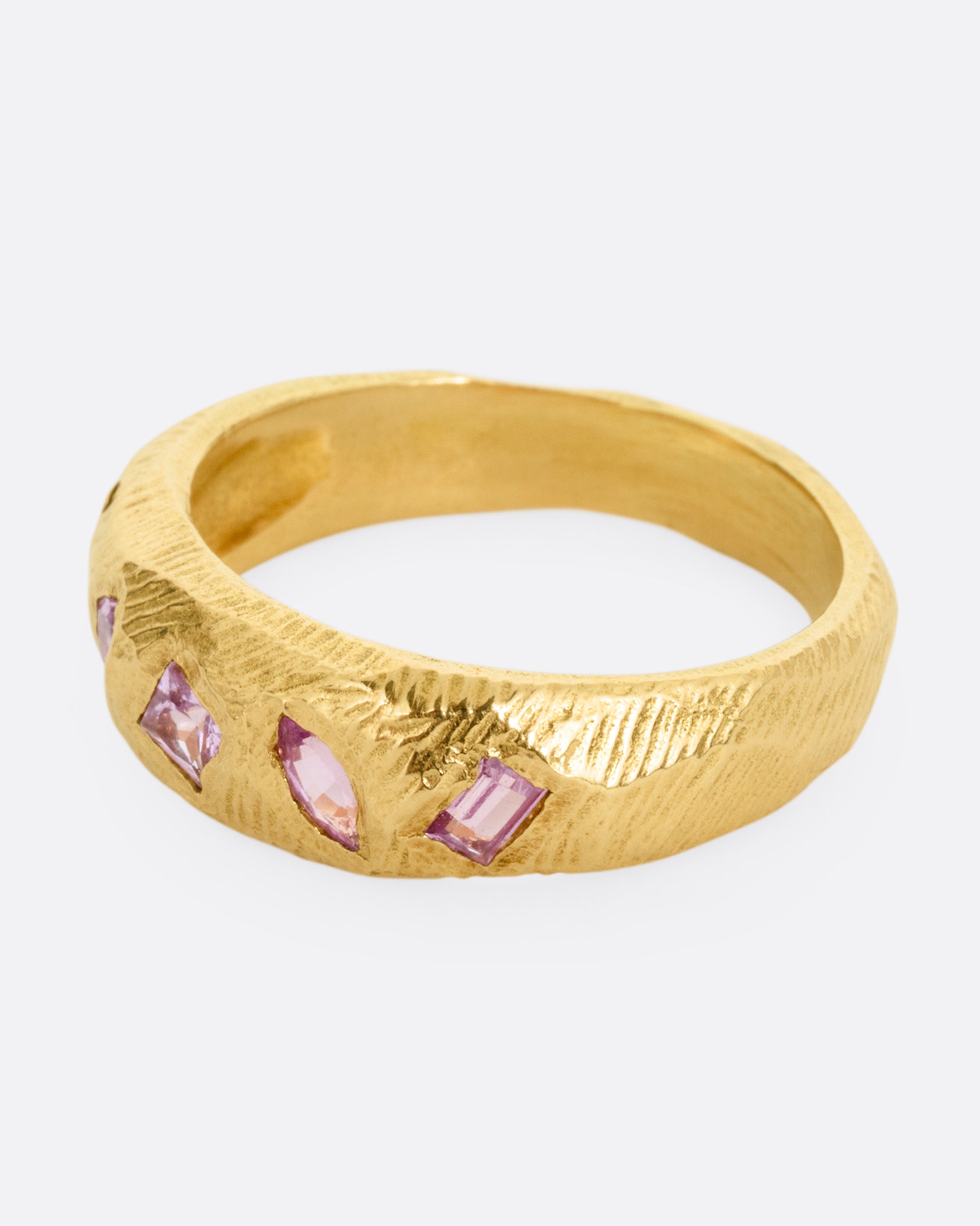 A yellow gold band with five pink sapphires, shown from the side.