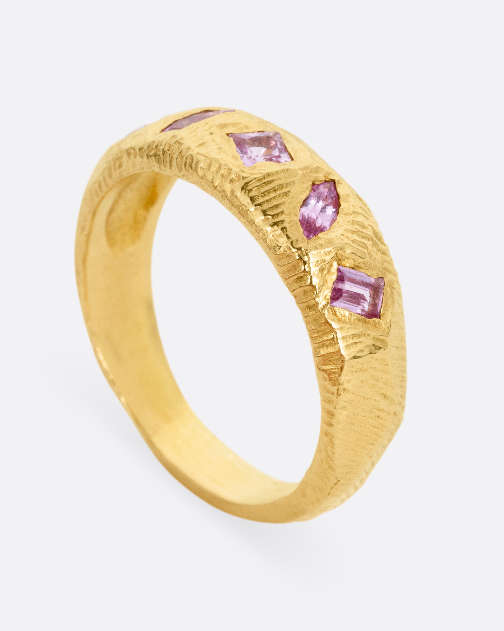 A yellow gold band with five pink sapphires, shown standing up  from the side.
