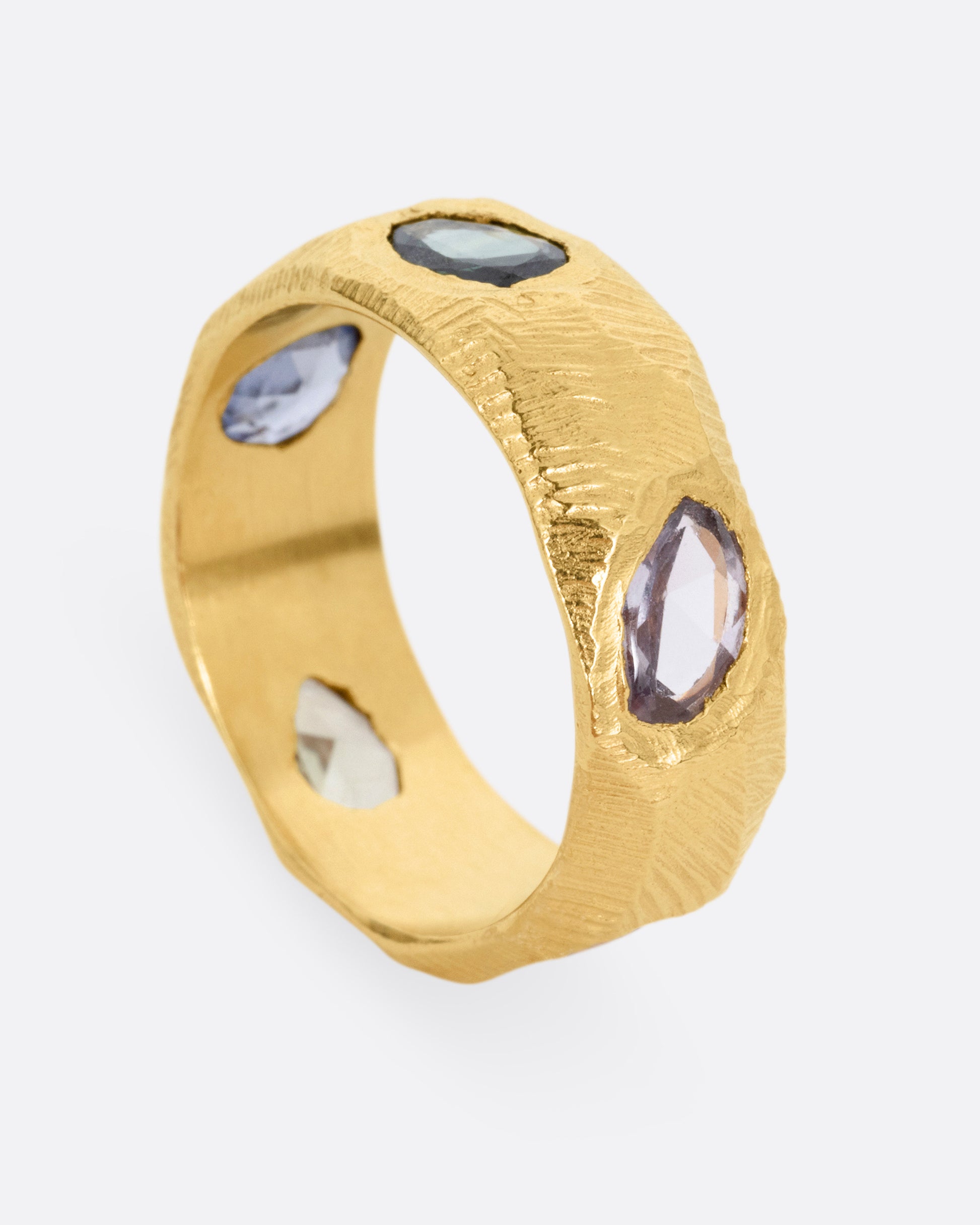 A yellow gold ring with rose cut sapphires in cool blues and greens, shown standing up from the side.