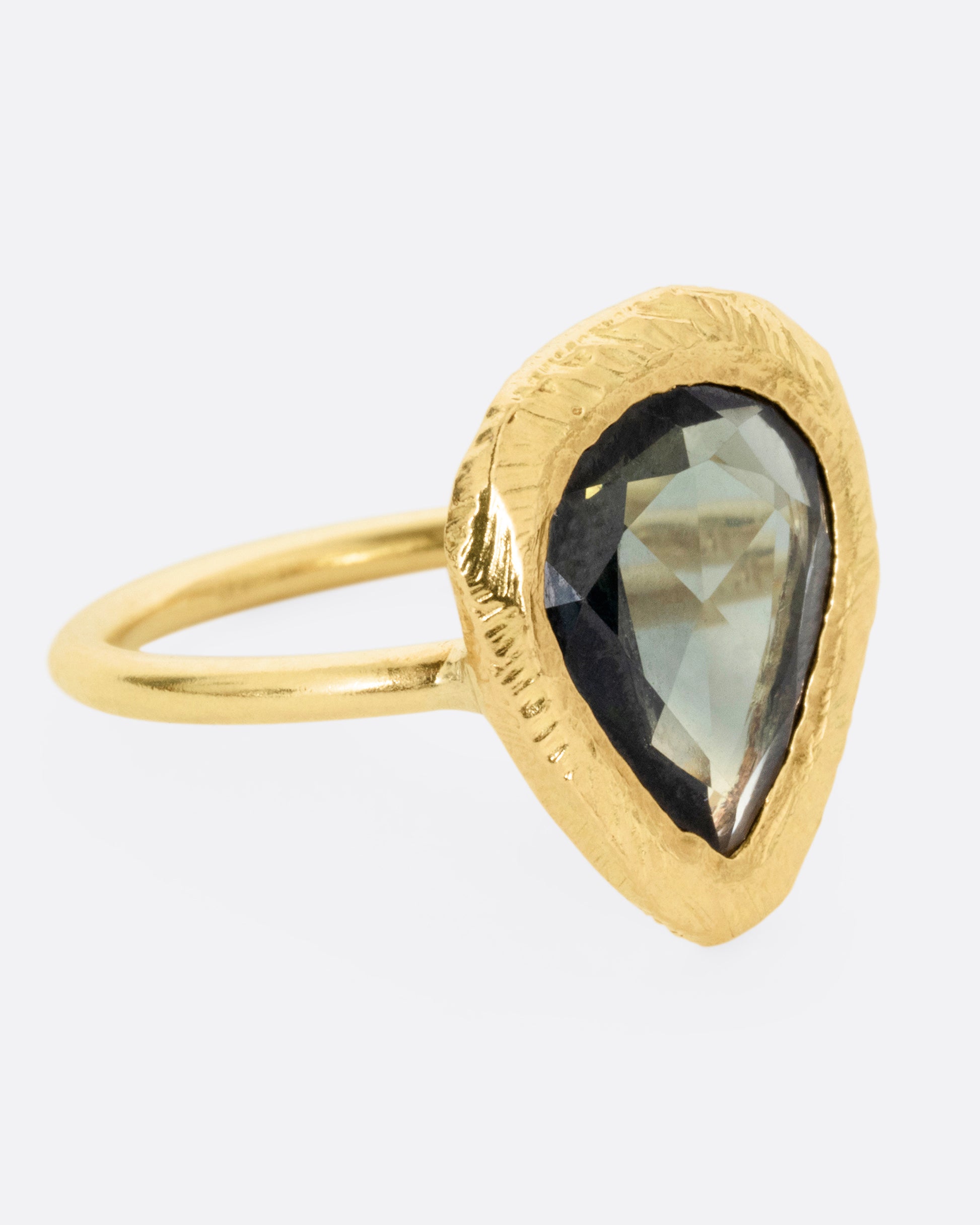 A yellow gold ring with a large sage green sapphire, shown from the side.
