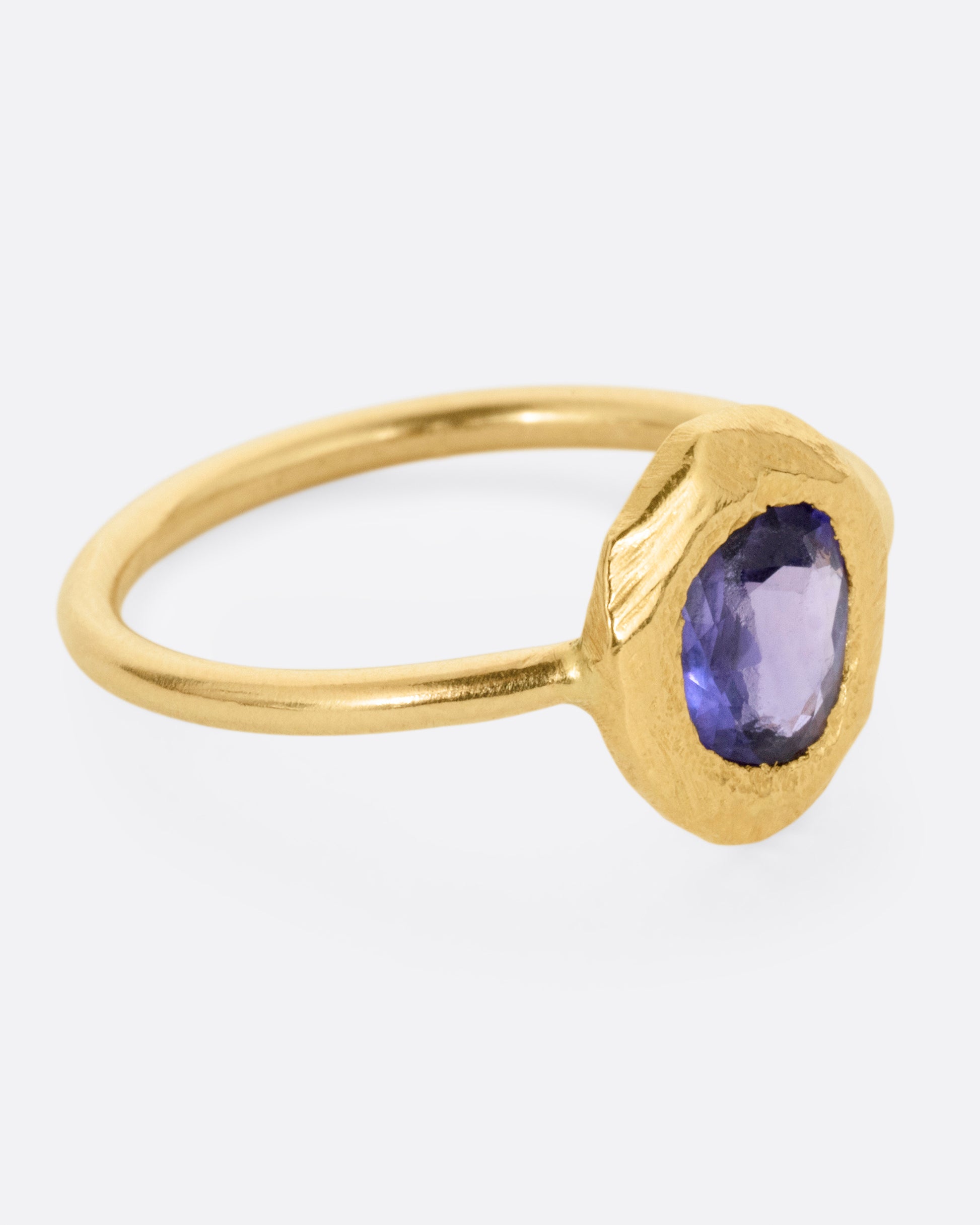 A yellow gold ring with a purple blue sapphire, shown from the side.