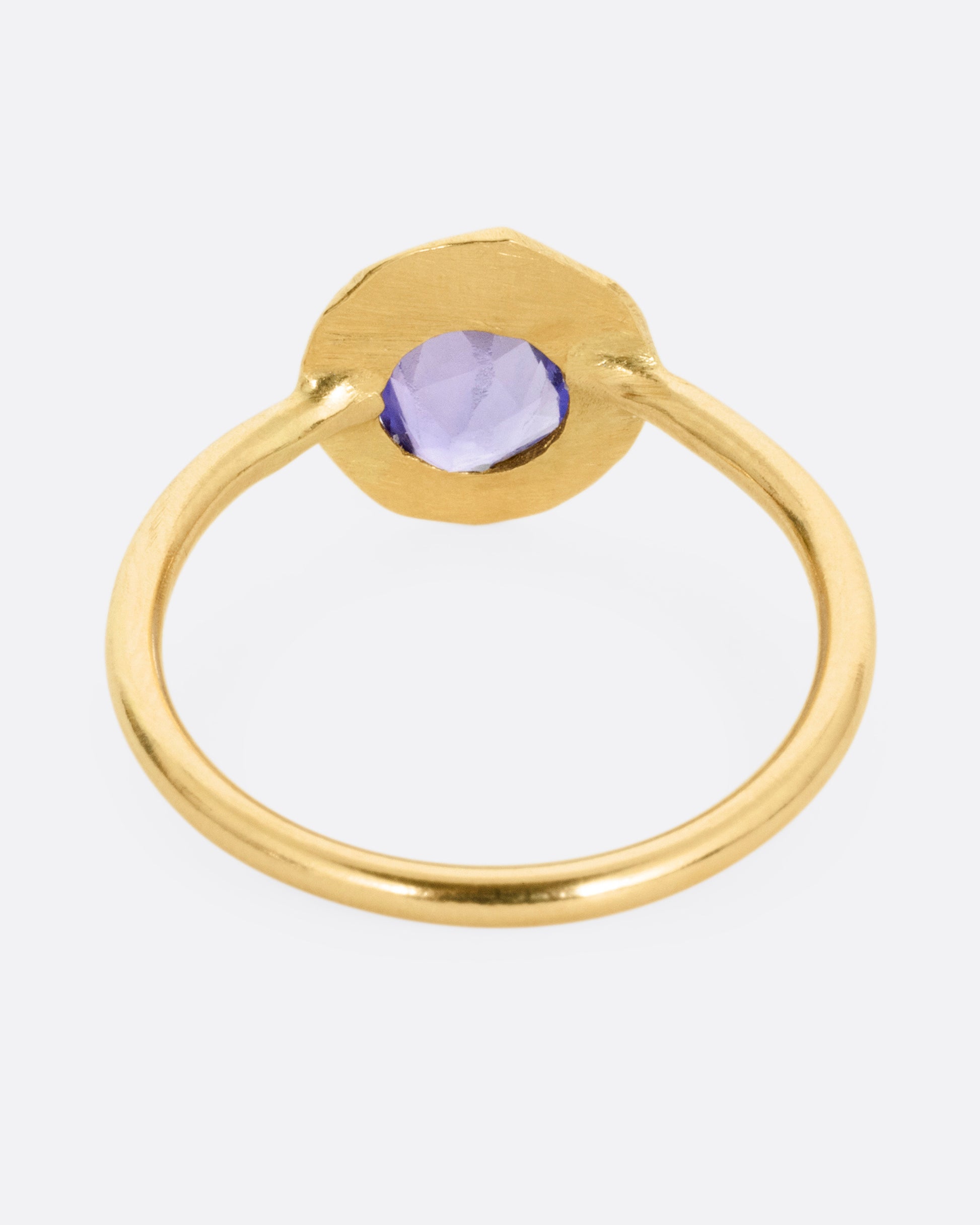 A yellow gold ring with a purple blue sapphire, shown from the back.