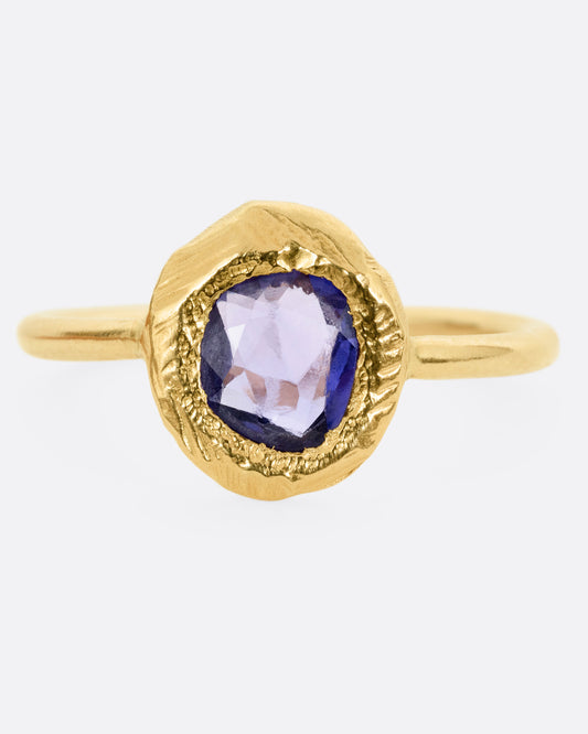 A yellow gold ring with a purple blue sapphire, shown from the front.