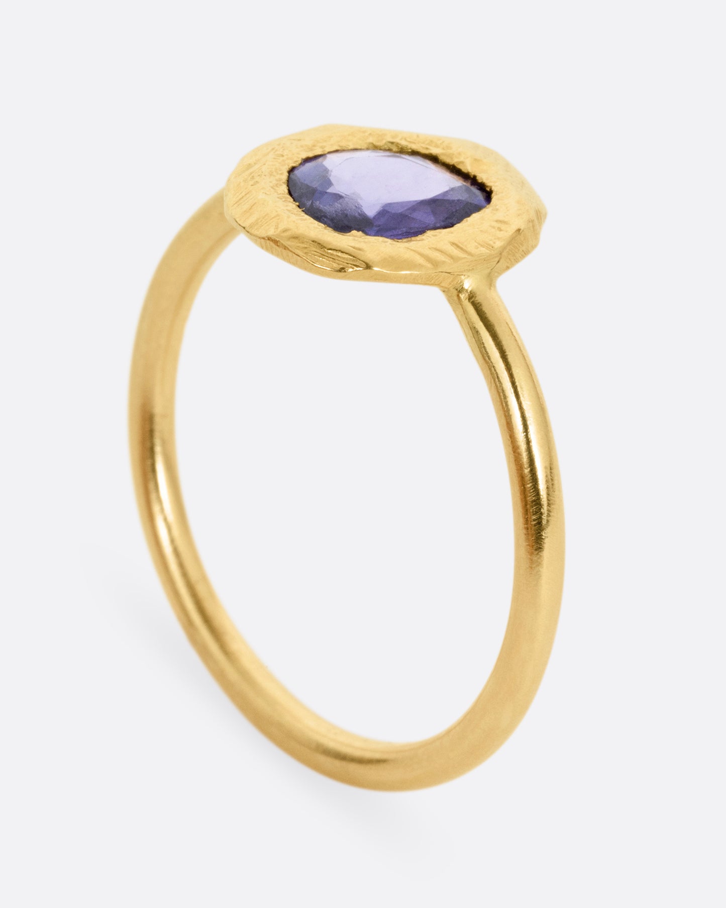 A yellow gold ring with a purple blue sapphire, shown from the side standing up.