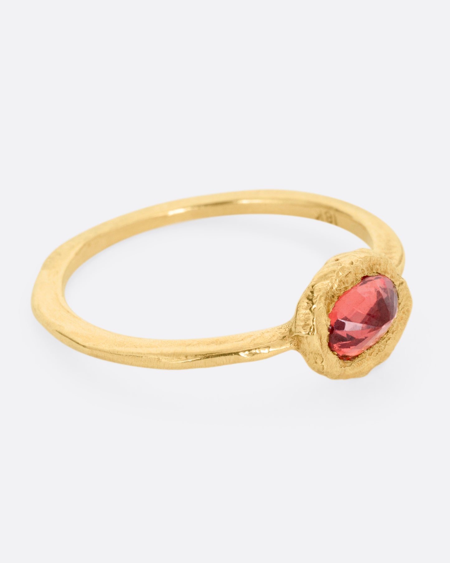 A yellow gold ring with a poppy red sapphire bezel set in a hand carved band. Shown from the side.