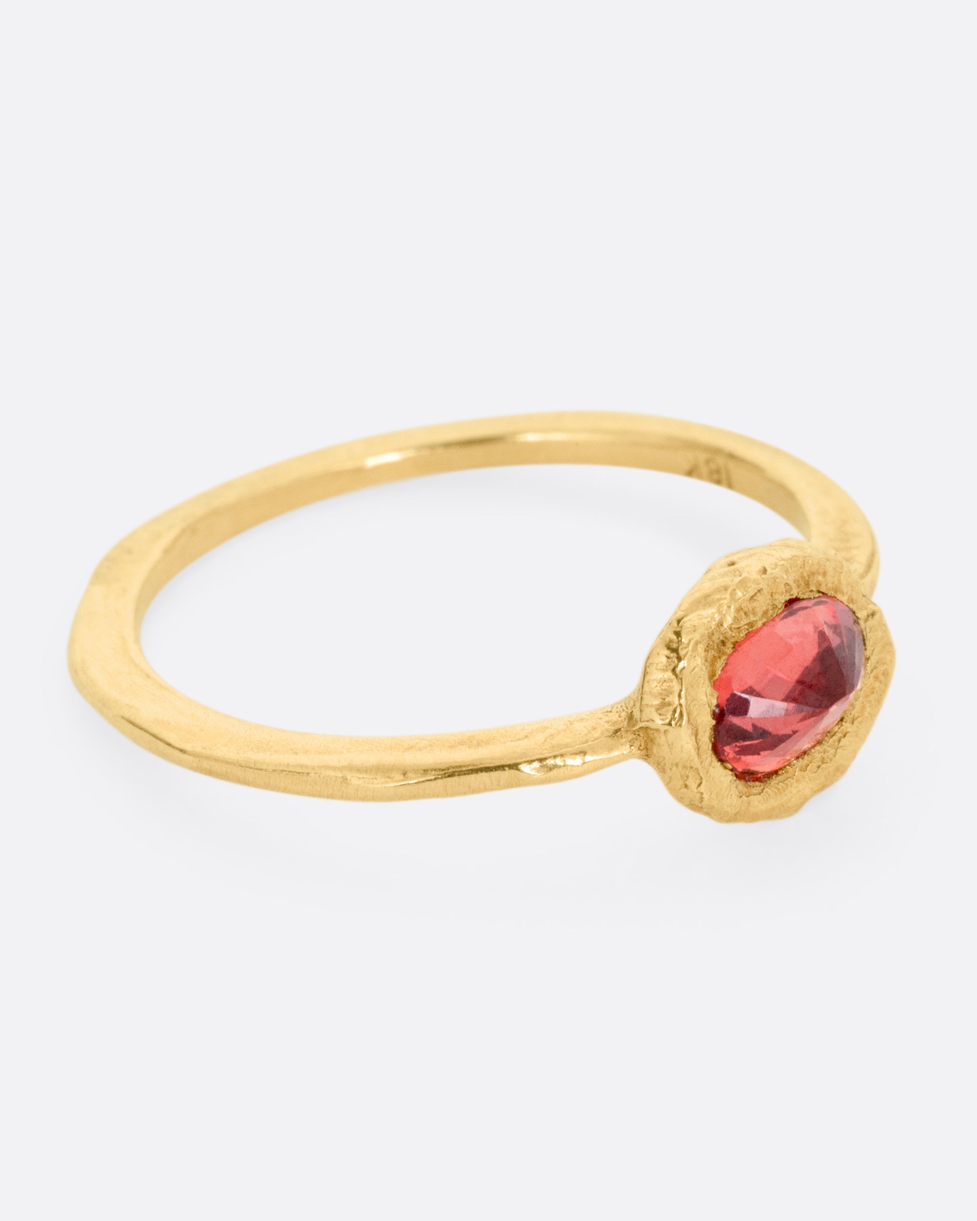 A yellow gold ring with a poppy red sapphire bezel set in a hand carved band. Shown from the side.