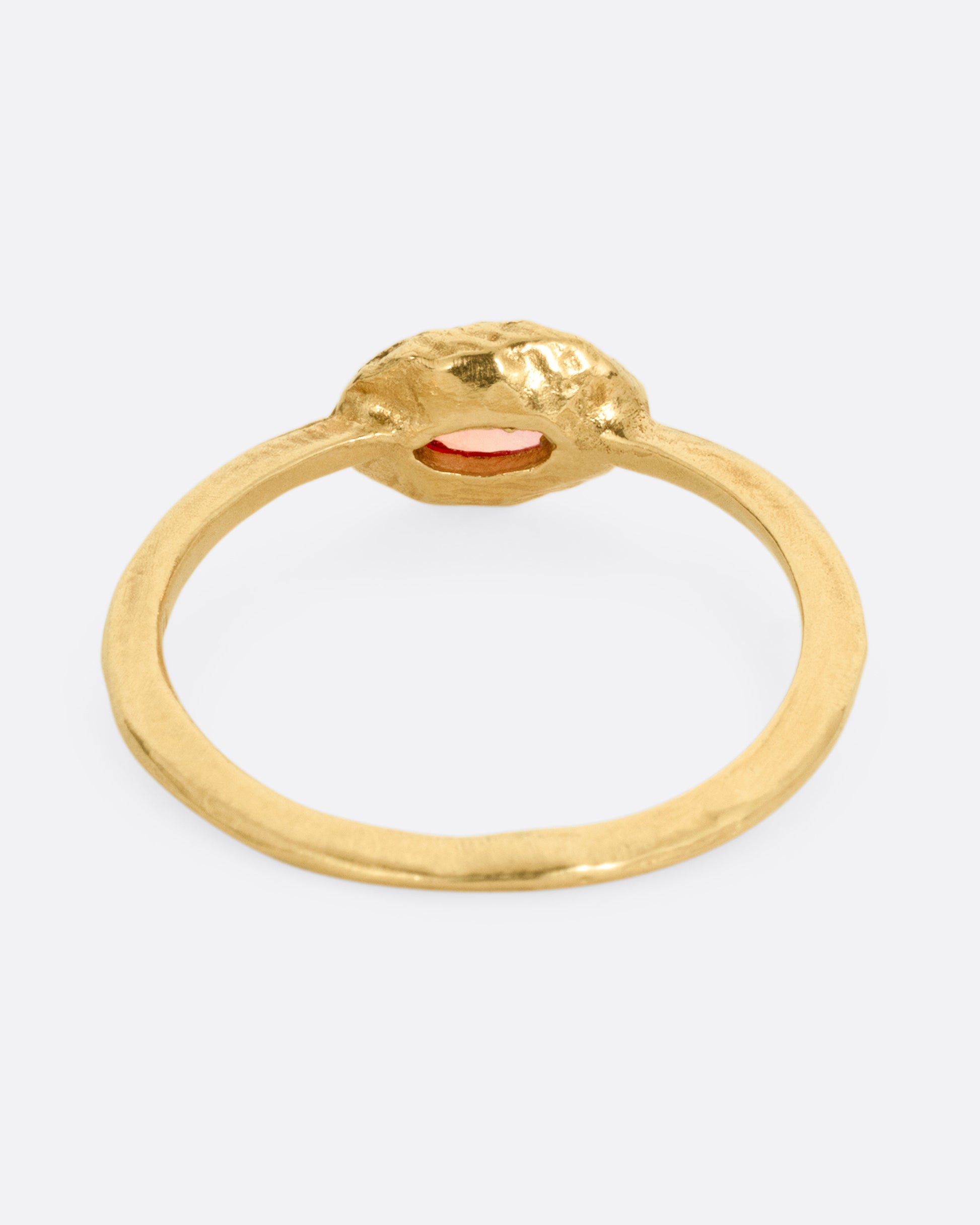 A yellow gold ring with a poppy red sapphire bezel set in a hand carved band. Shown from the back.