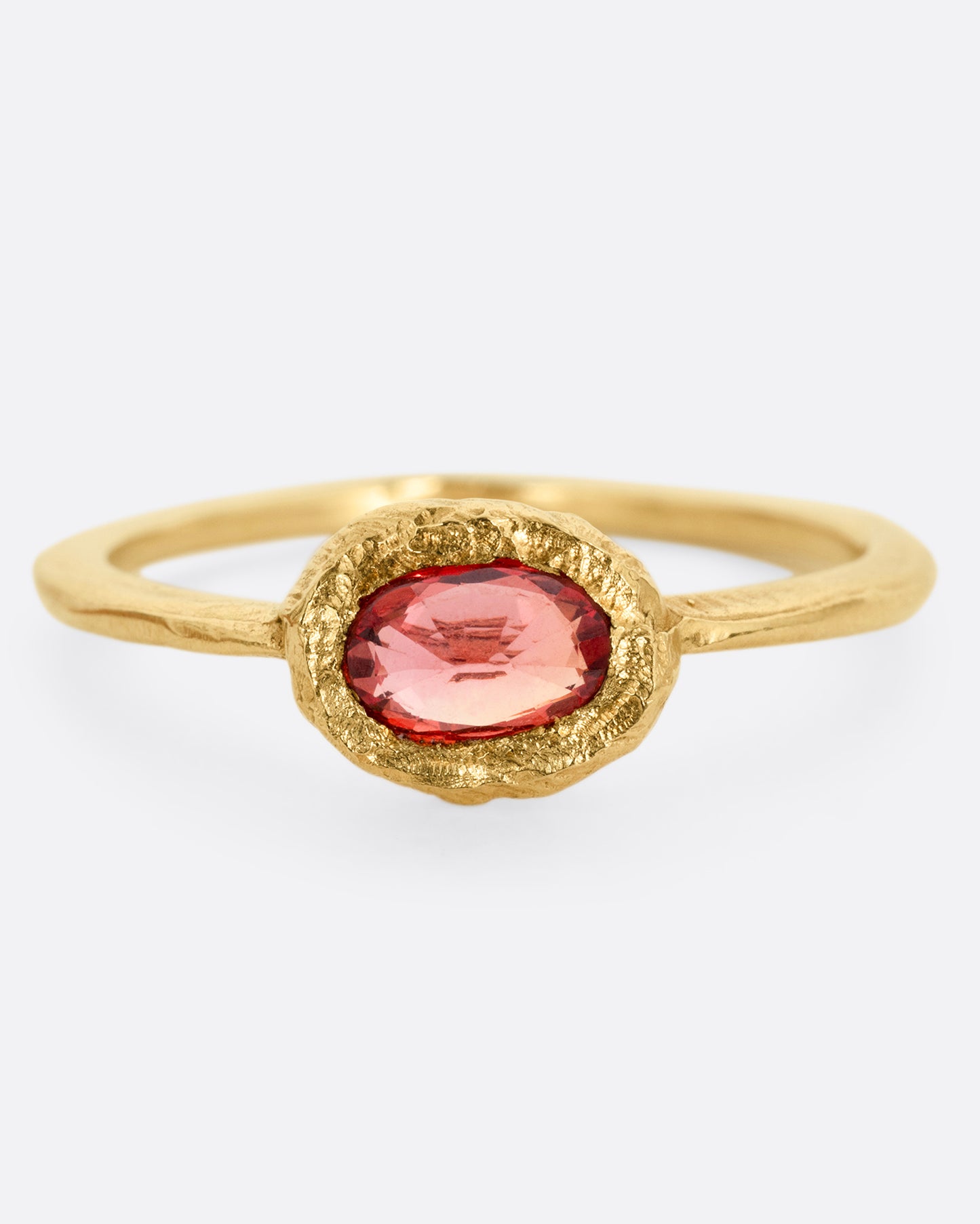 A yellow gold ring with a poppy red sapphire bezel set in a hand carved band. Shown from the front.