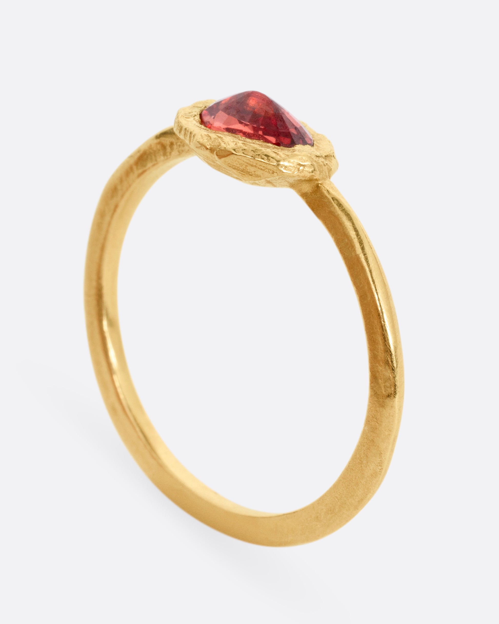 A yellow gold ring with a poppy red sapphire bezel set in a hand carved band. Shown standing up from the side.