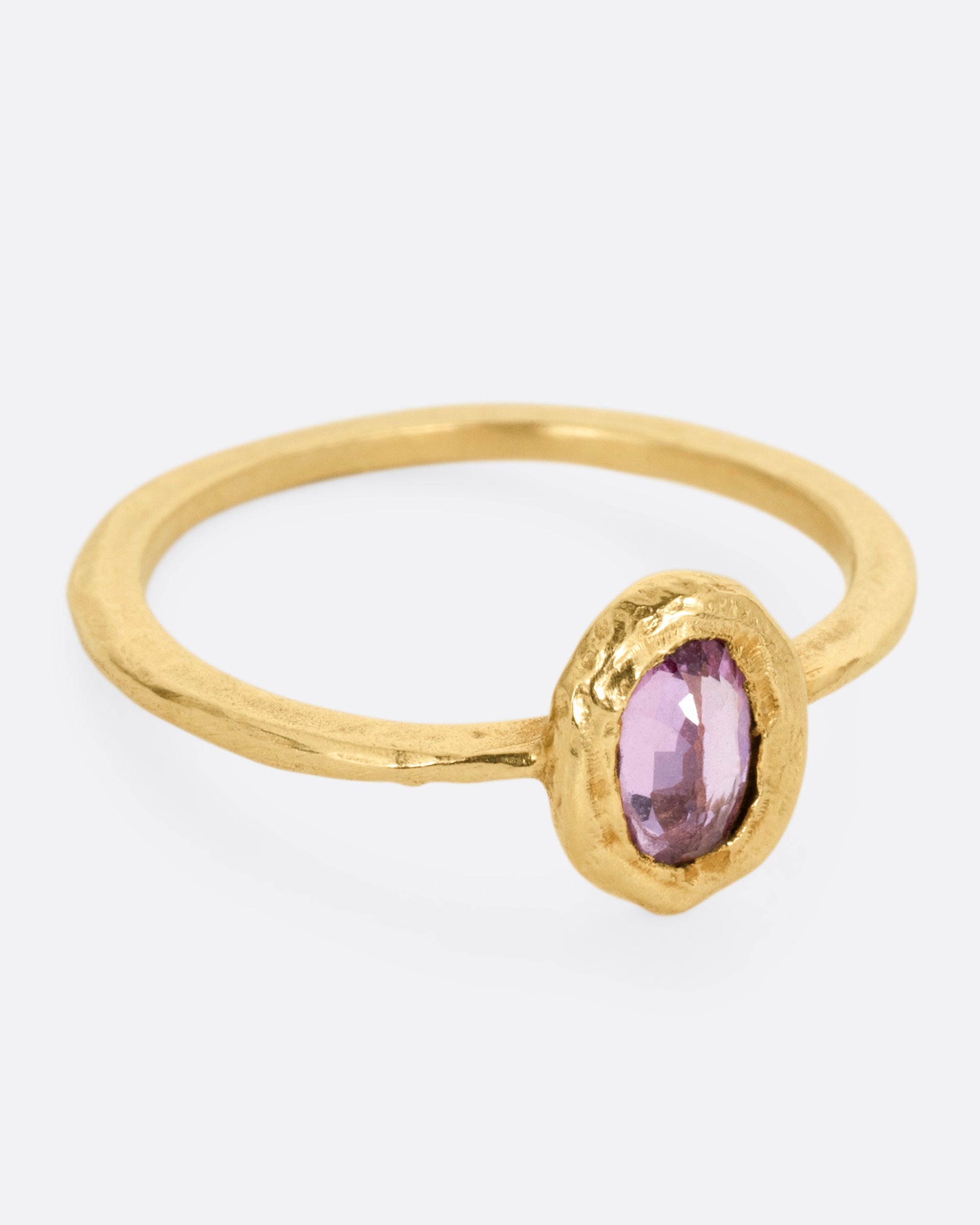 A yellow gold ring with a  pale pink sapphire in a hand carved bezel. Shown from the side.