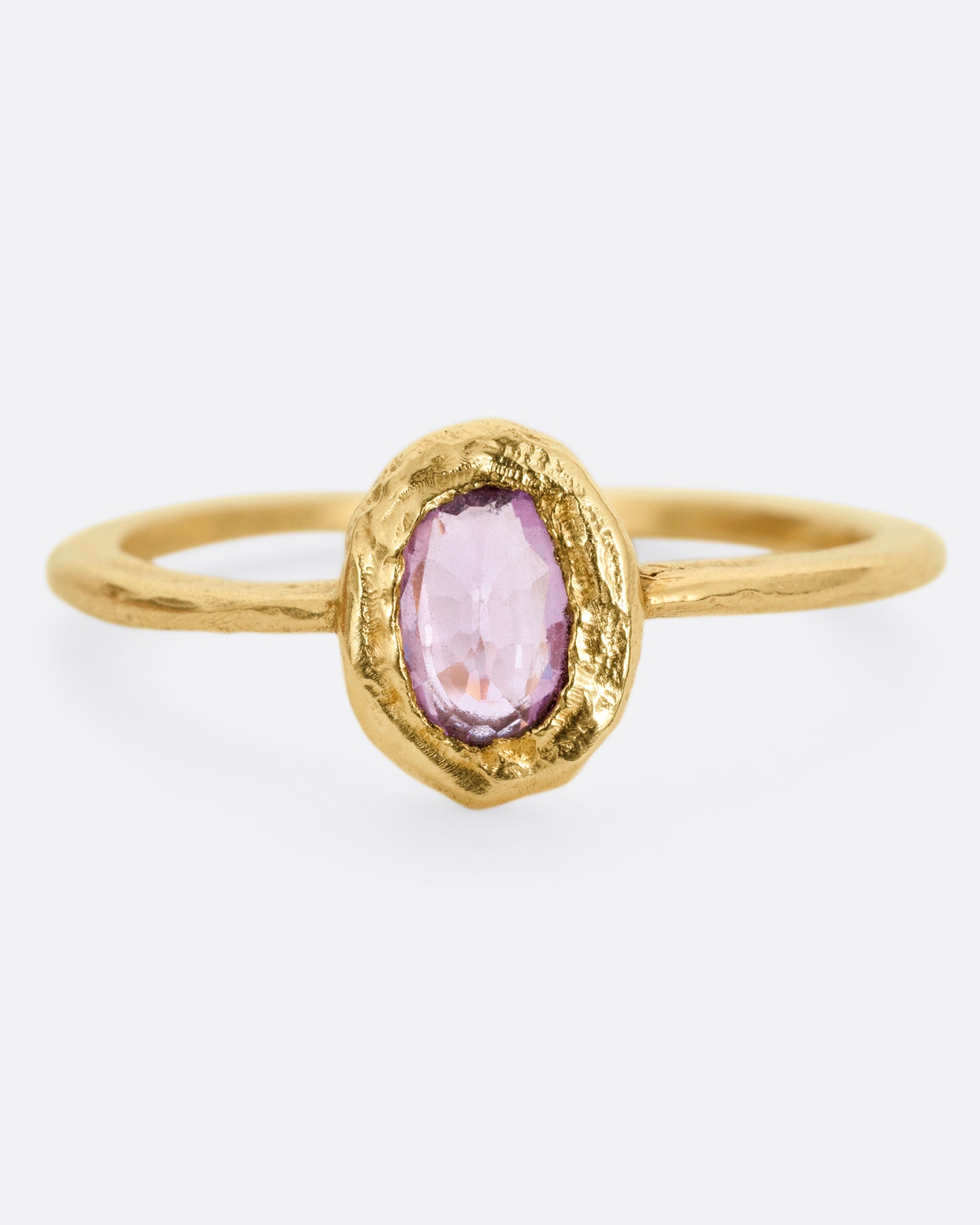 A yellow gold ring with a  pale pink sapphire in a hand carved bezel. Shown from the front.