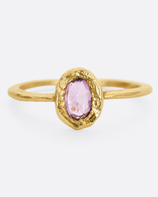 A yellow gold ring with a  pale pink sapphire in a hand carved bezel. Shown from the front.