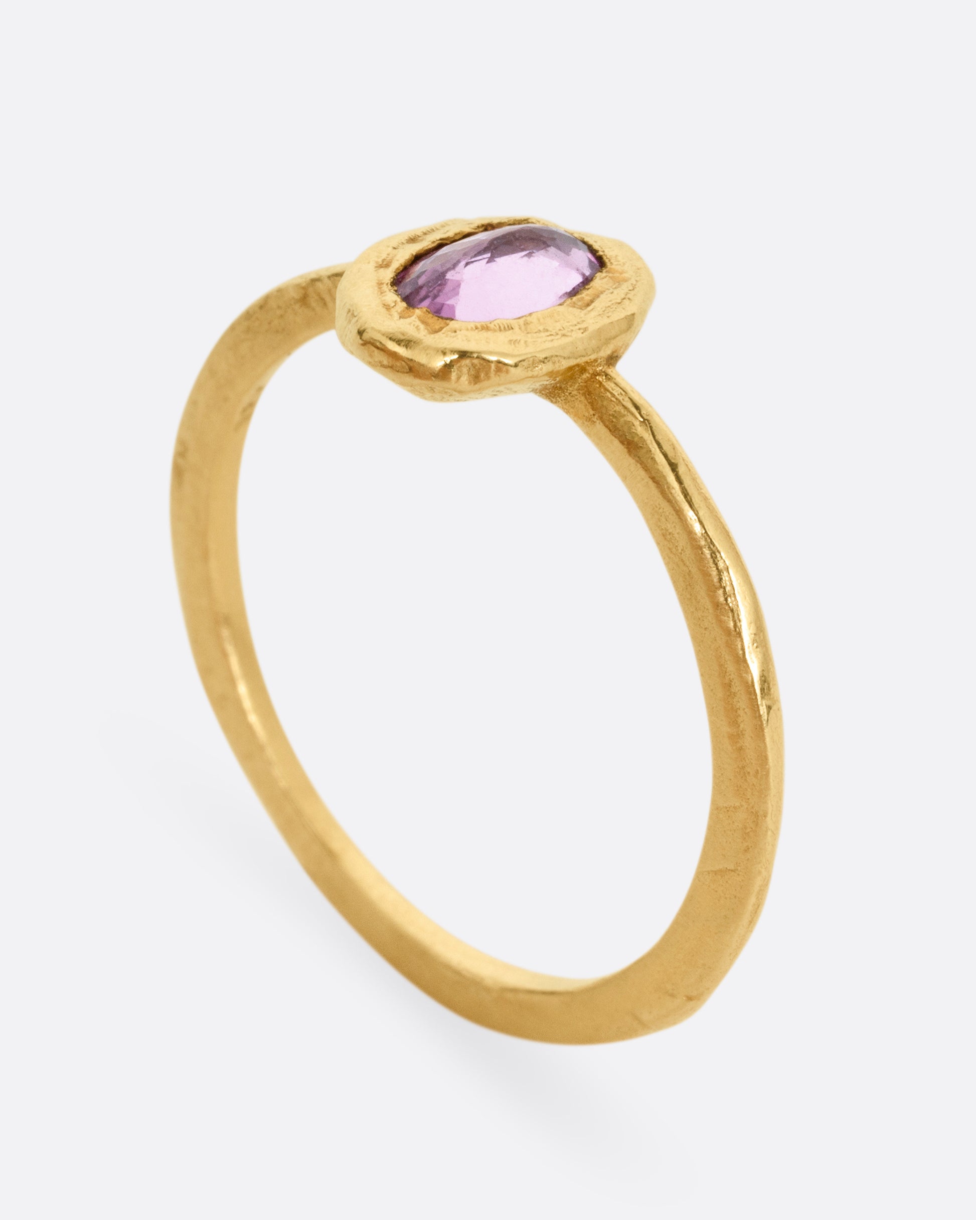 A yellow gold ring with a  pale pink sapphire in a hand carved bezel. Shown from the side standing up.