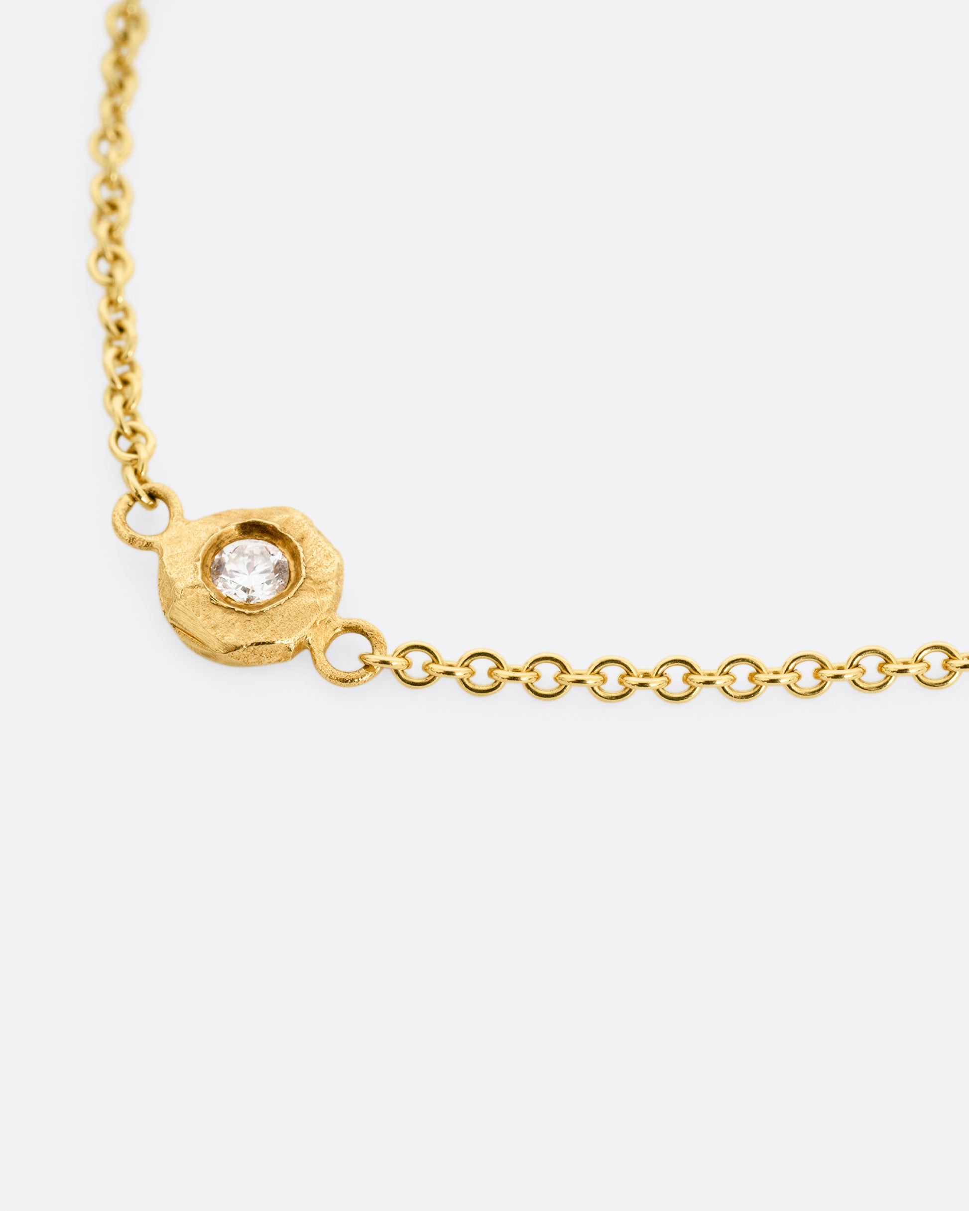 A close up of a yellow gold cable chain necklace with five diamonds set in hand carved bezels. 
