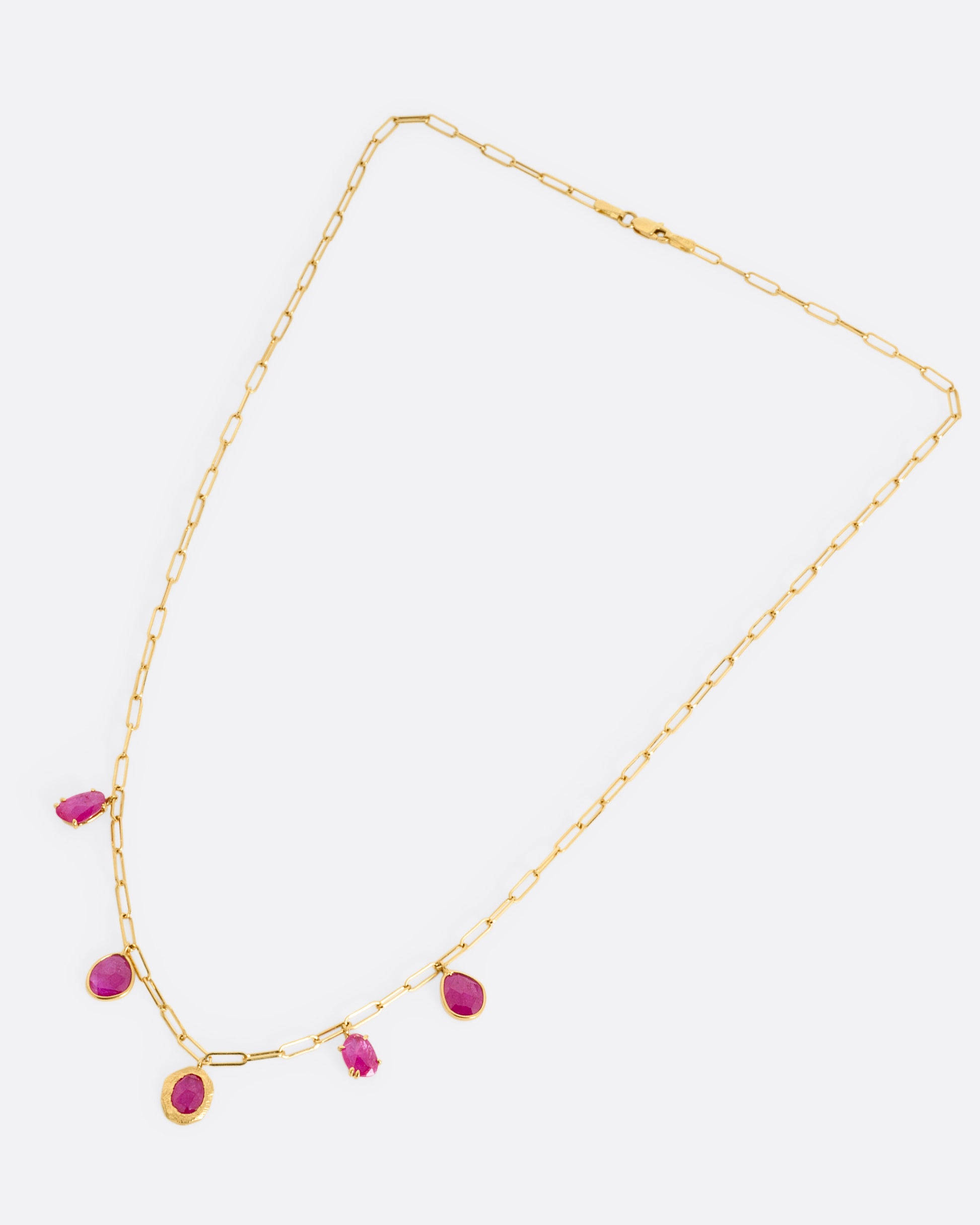 A yellow gold staple chain necklace with five rose cut ruby charms. Shown from the front.