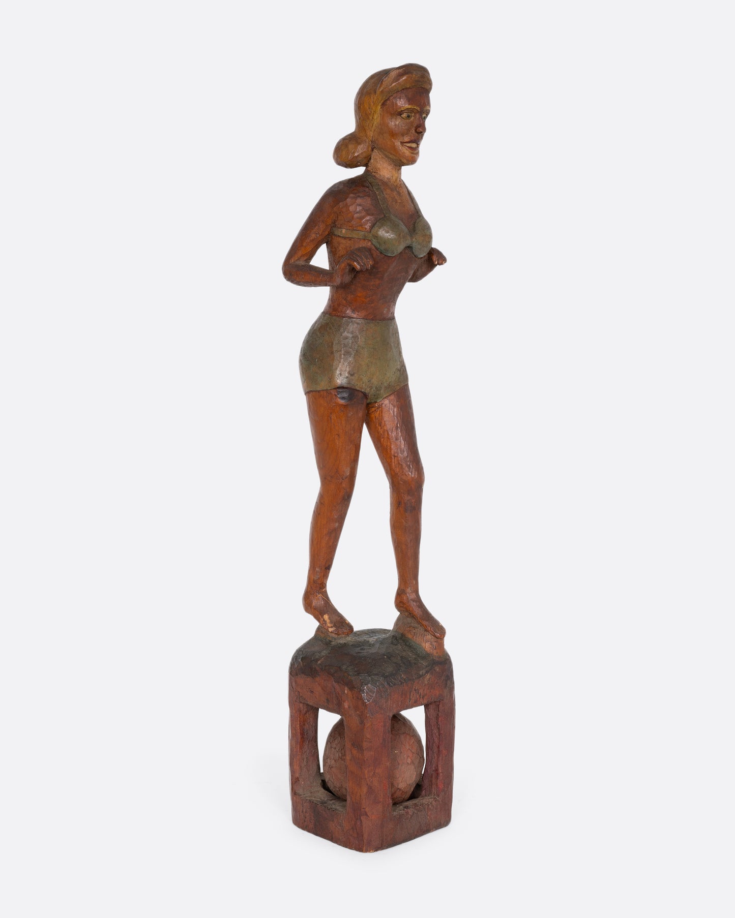 A hand carved wooden whimsy, a woman in a swimsuit standing on a ball. Shown from the side.