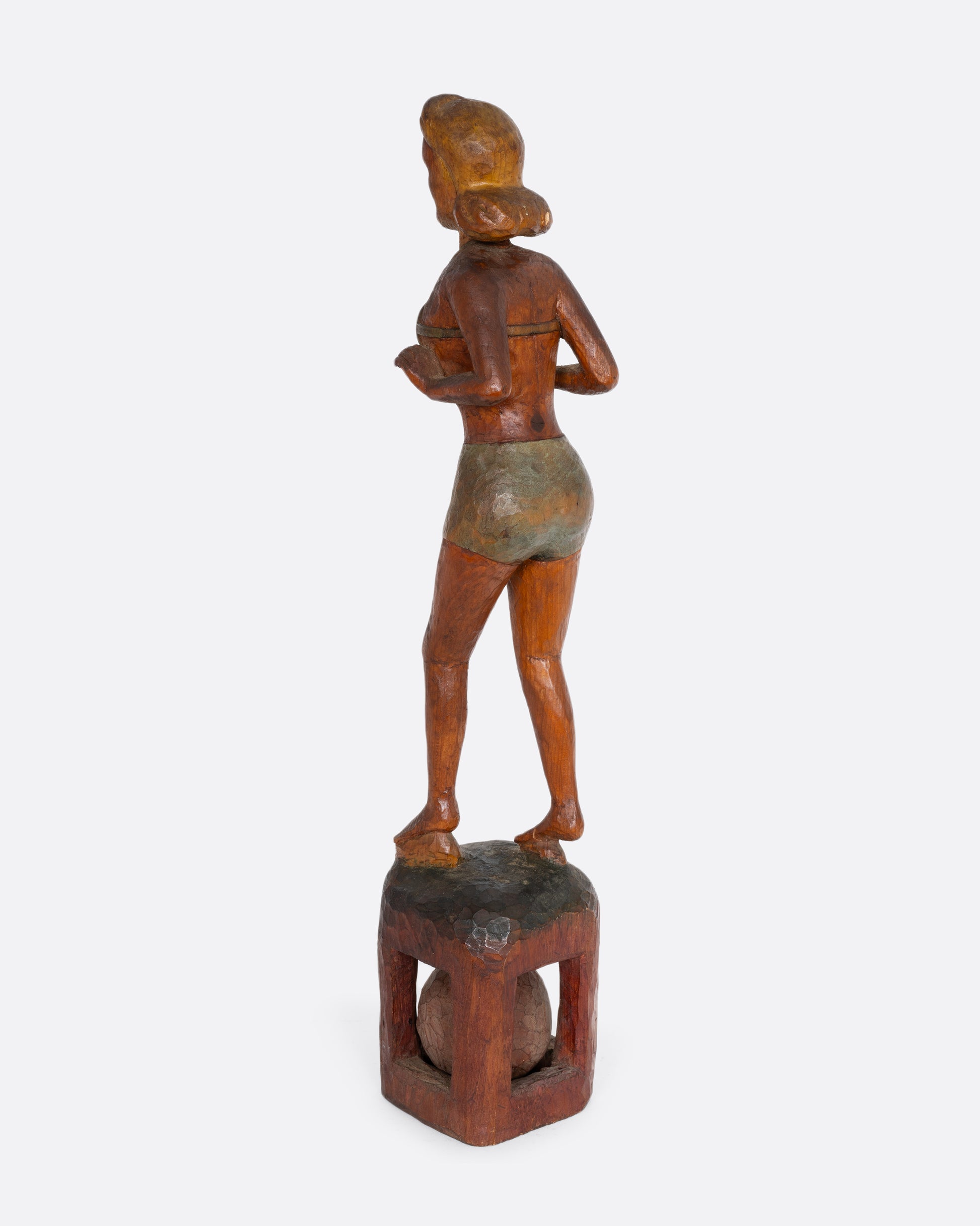 A hand carved wooden whimsy, a woman in a swimsuit standing on a ball. Shown from the back.