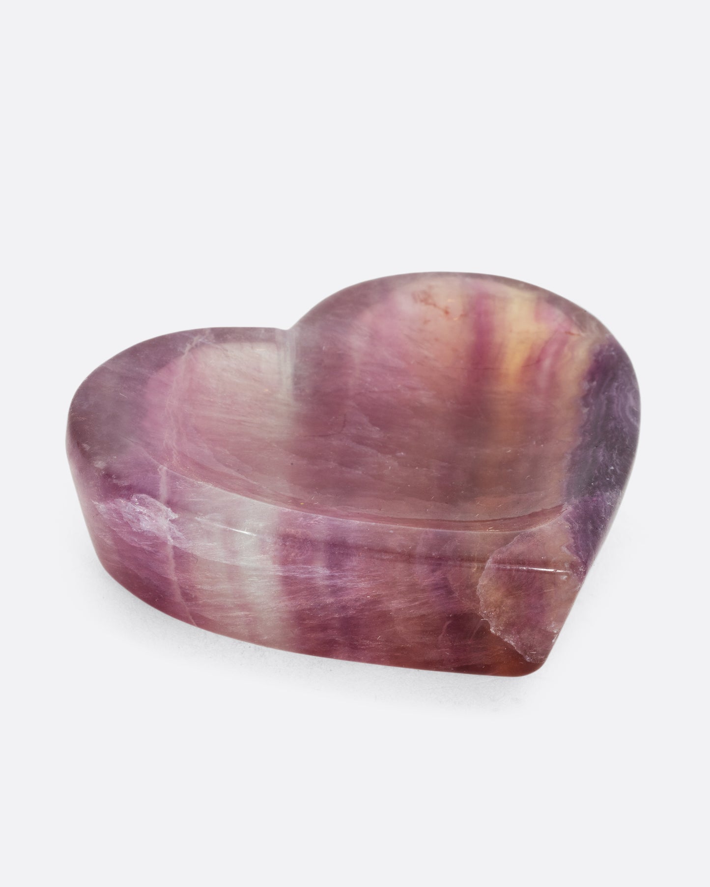 A flourite stone bowl in the shape of a heart. Shown laying flat on a table.