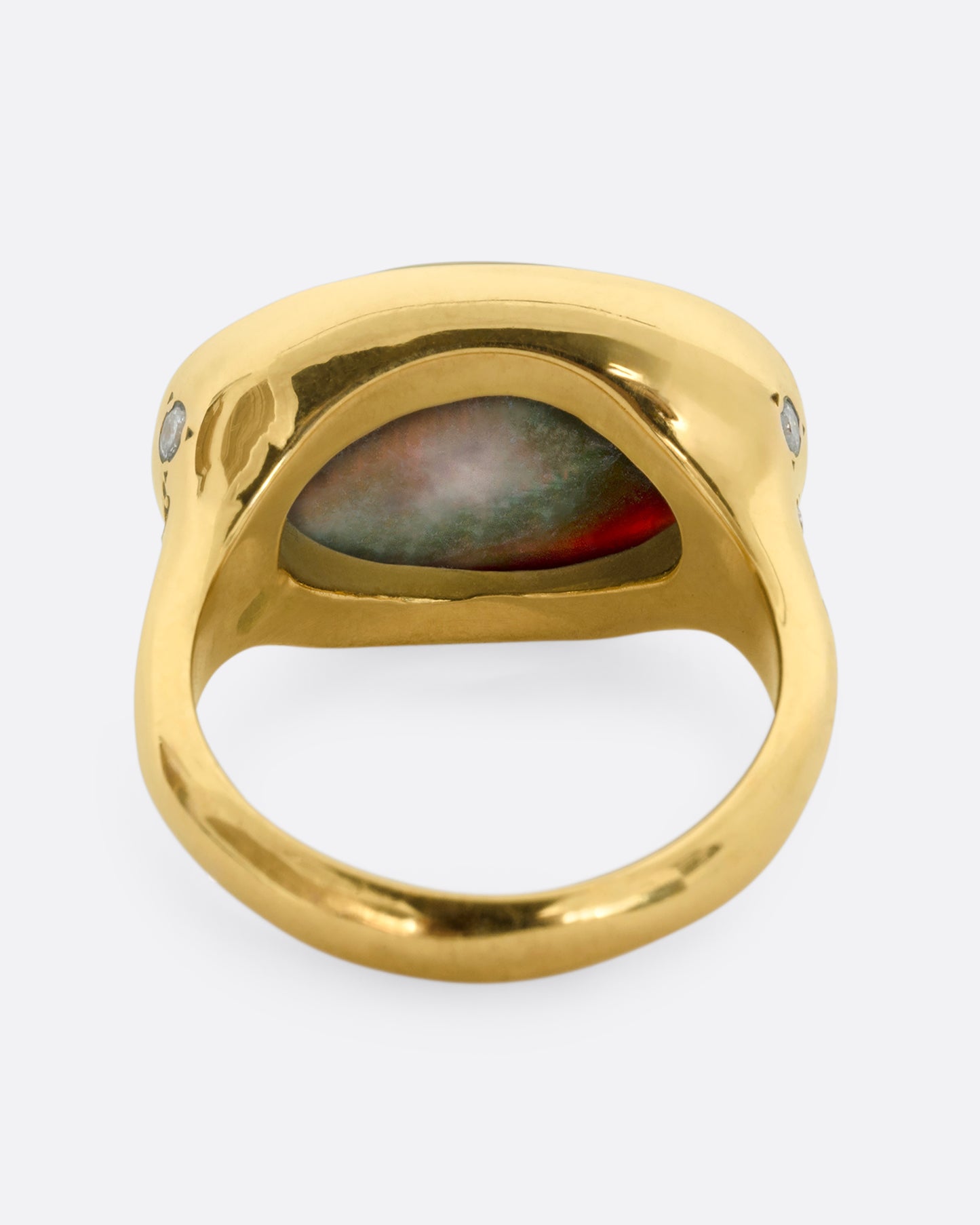 A yellow gold ring with a large oval opal at the center and diamonds on either shoulder. View from the back.