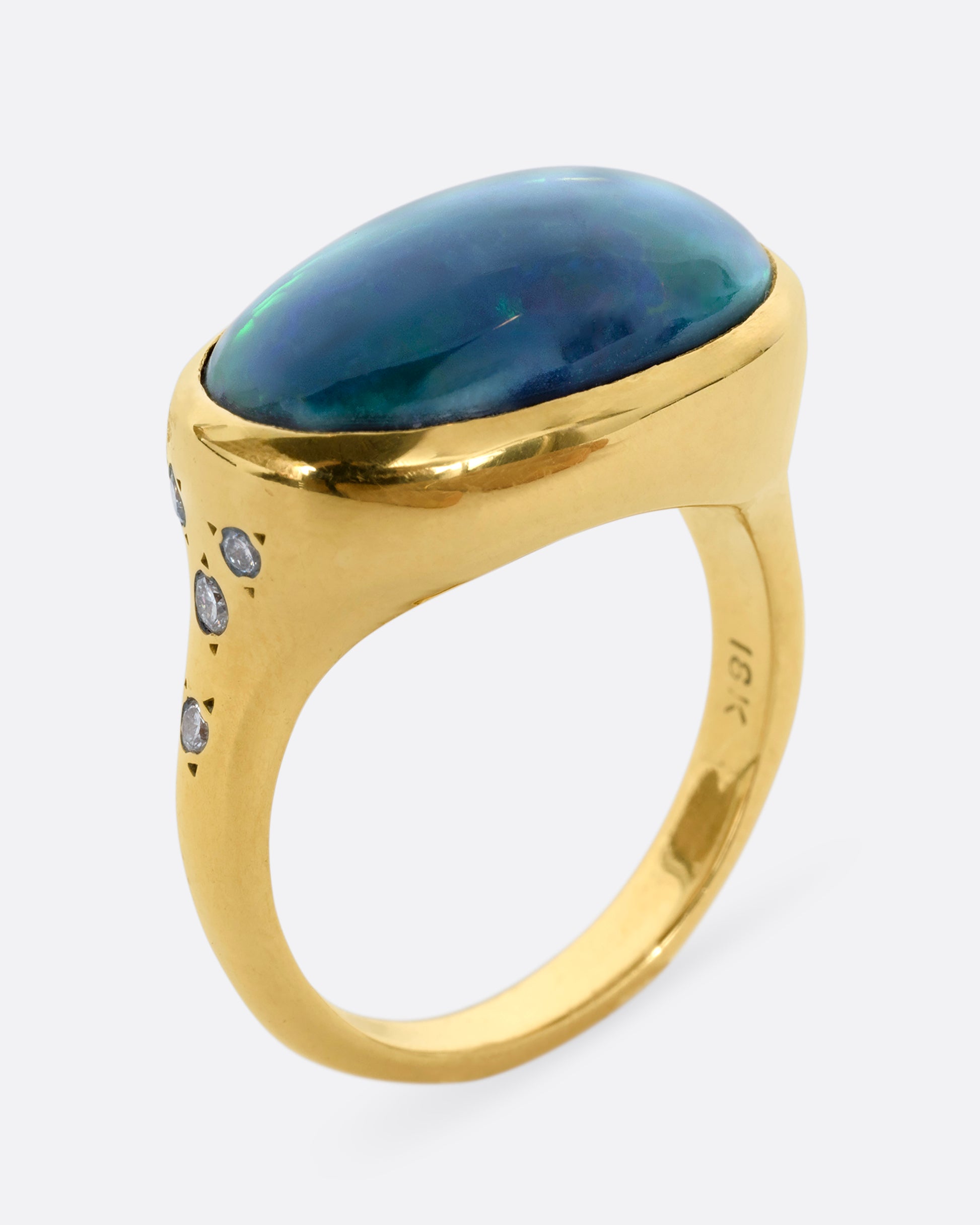 A yellow gold ring with a large oval opal at the center and diamonds on either shoulder. View from the side, standing.