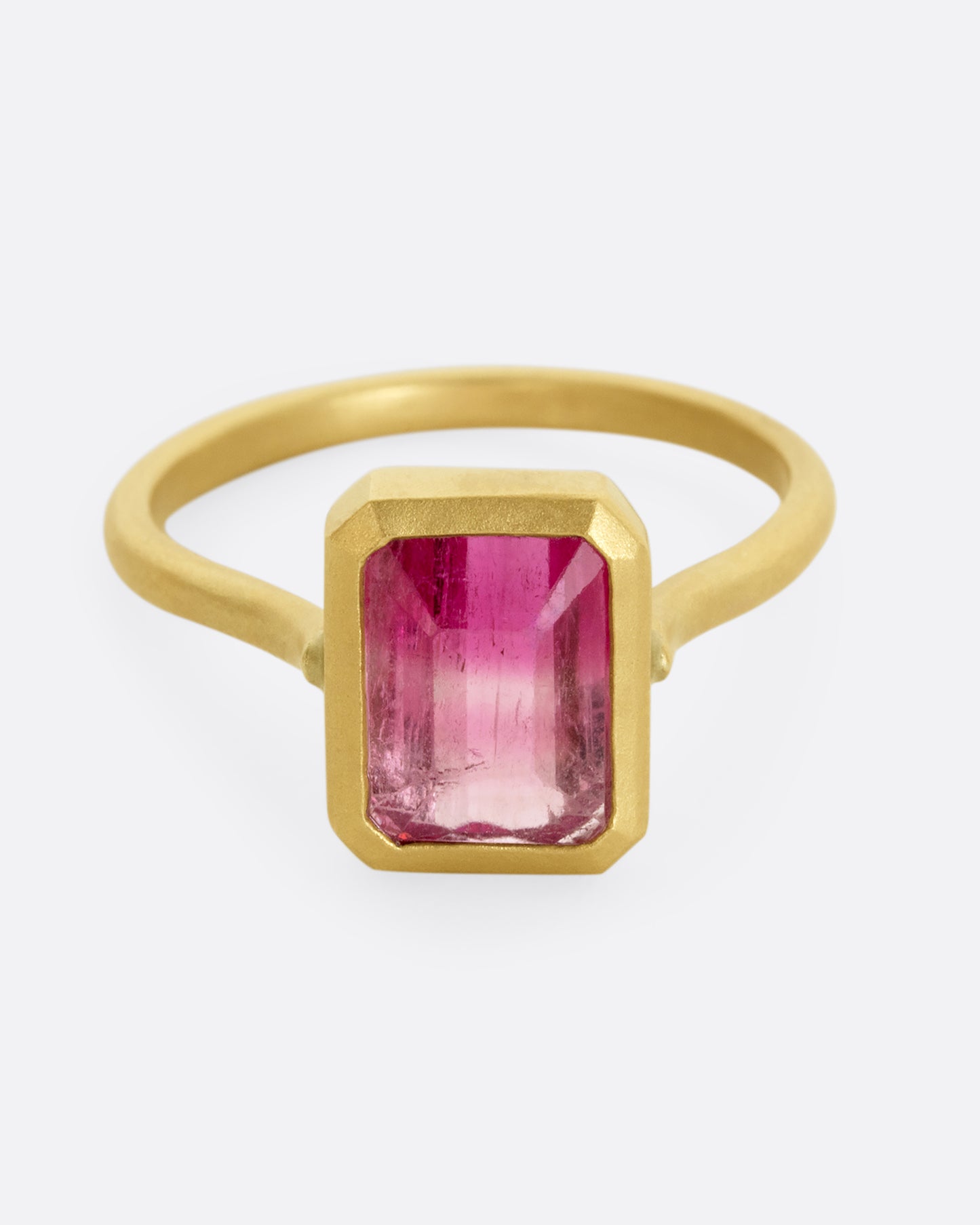 A yellow gold ring with a bezel set rectangular pink bicolor tourmaline. Shown from the front.